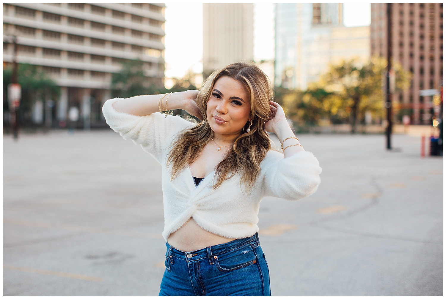 high school senior girl in cream top with hands on head standing in parking lot Houston downtown senior photos