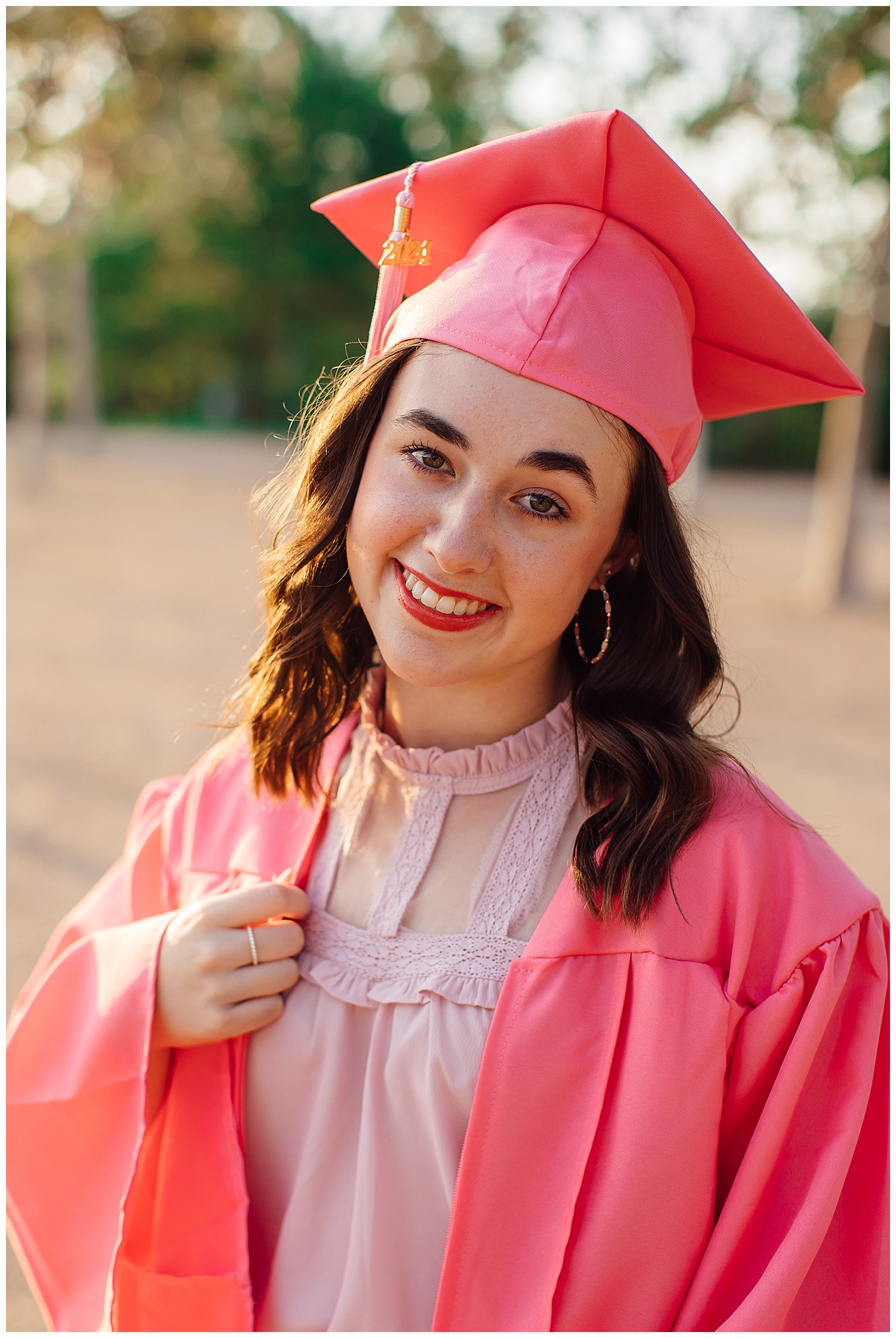 high school senior in pink graduation cap and gown posing outdoors Houston
