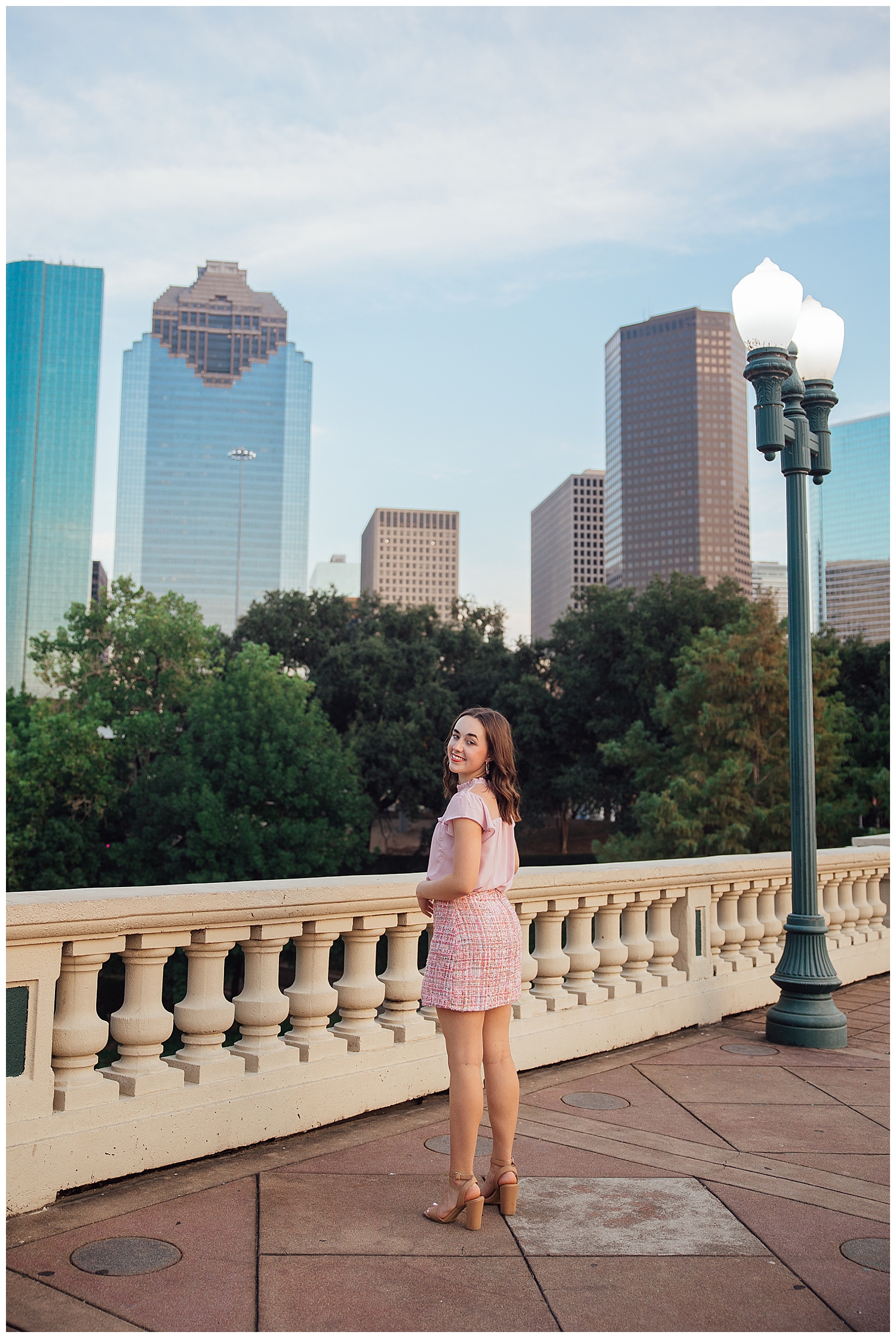 high school senior standing in on Sabine Street Bridge in pink skirt and pink shirt in front of Houston Skyline
