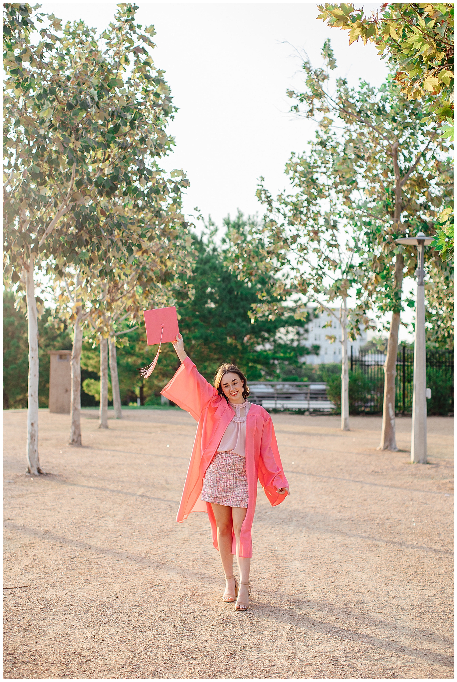 Houston Skyline Senior Photos with girl holding pink graduation cap up in the air while walking