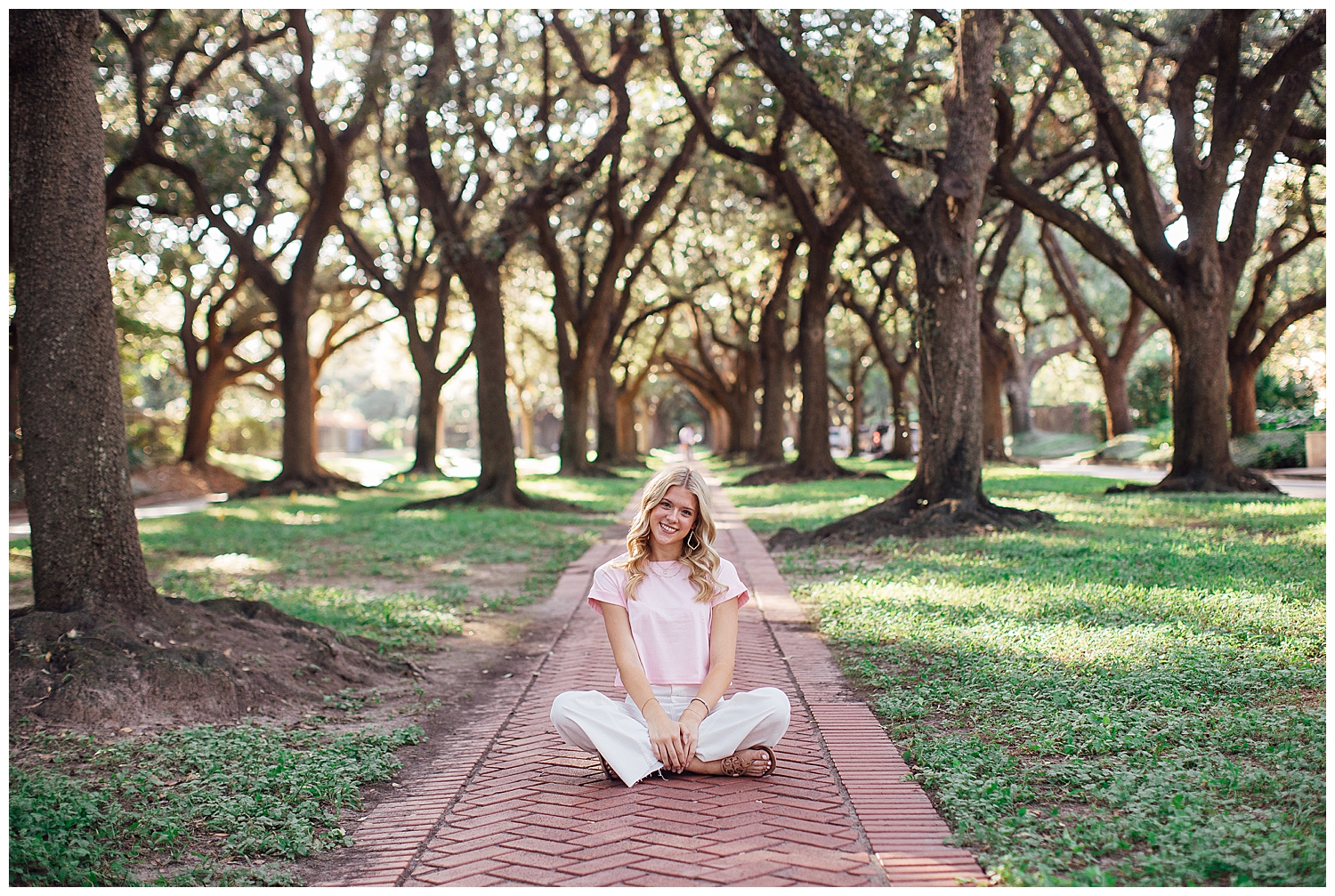 high school senior girl in white. pants pink shirt sitting on sidewalk senior photos Houston musuem district treeline