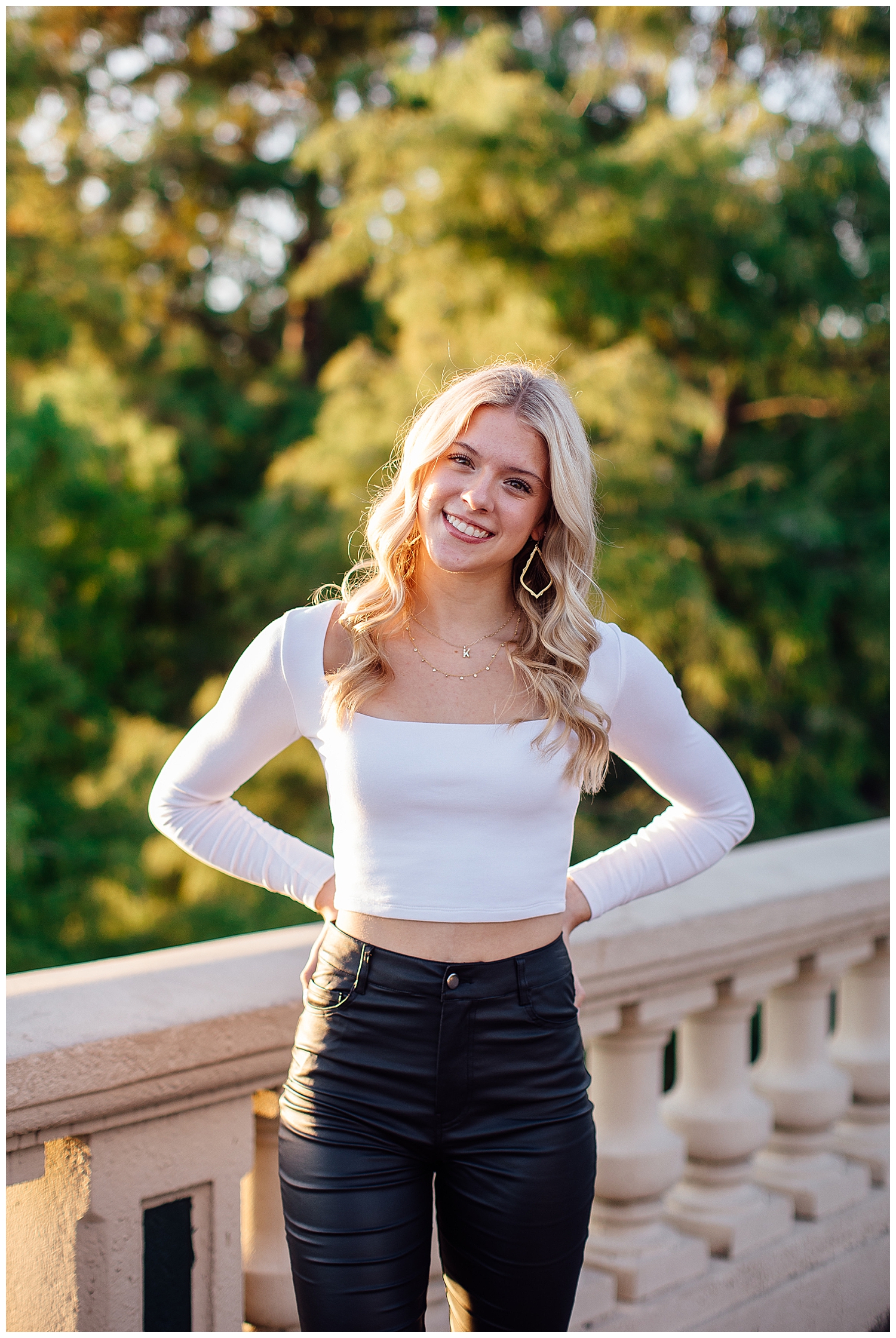 high school senior girl in white pants leaning against gray wall outdoors Buffalo Bayou houston
