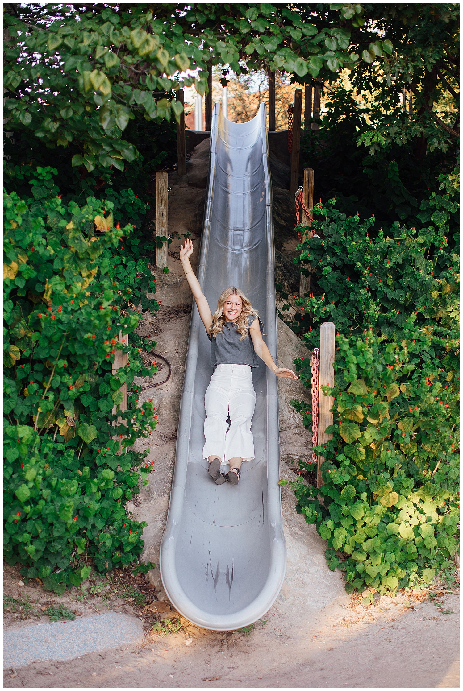 high school senior girl sliding down a slide with arms in air for fun senior photos Houston