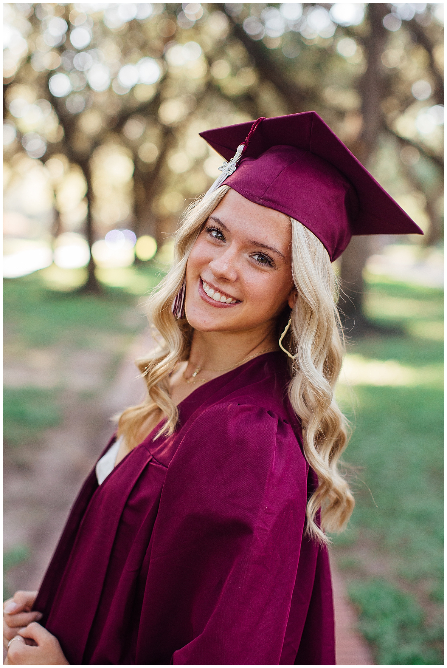 girl standing outdoors smiling wearing maroon graduation cap and gown