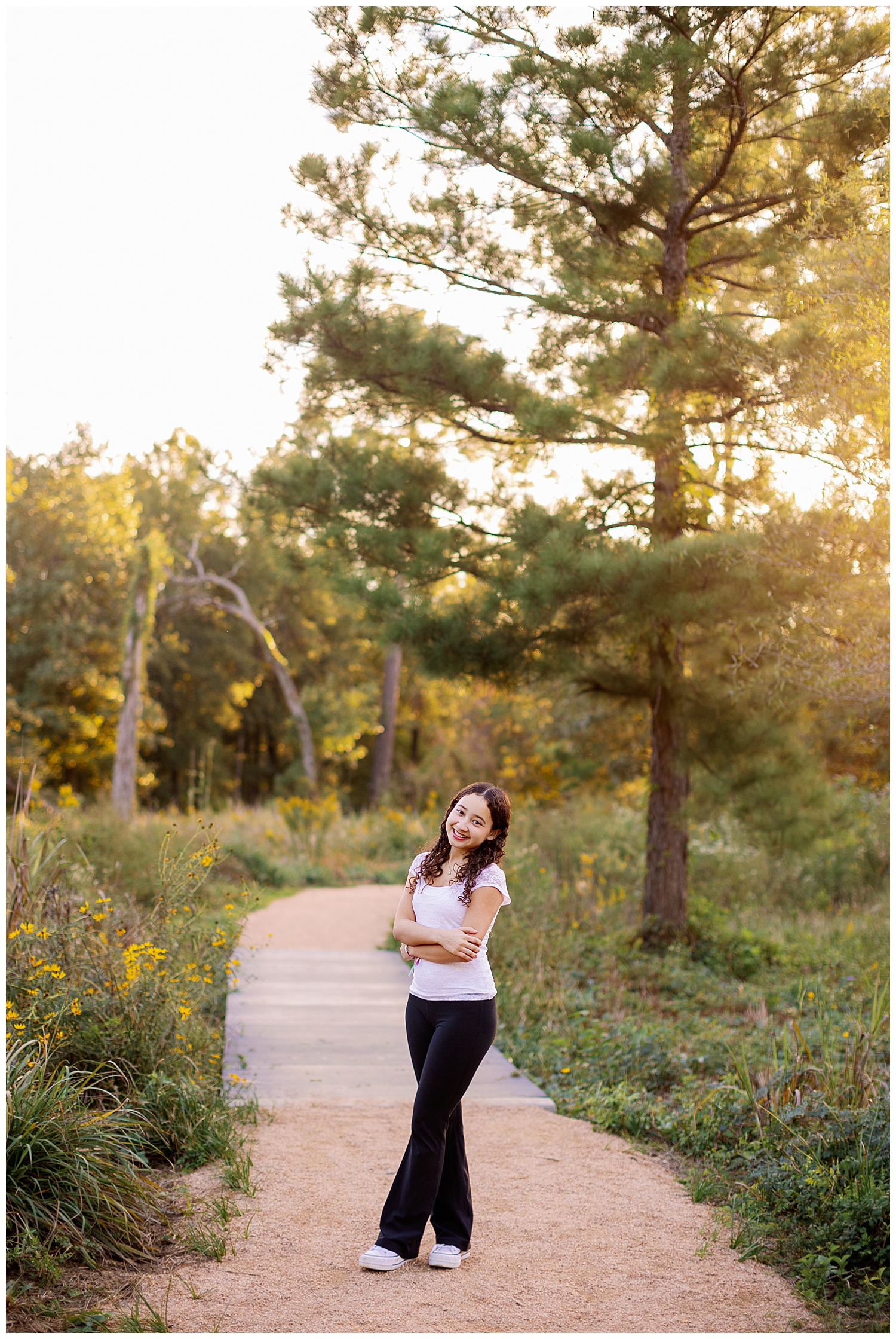 girl in jeans and white shirt standing on pathway with trees