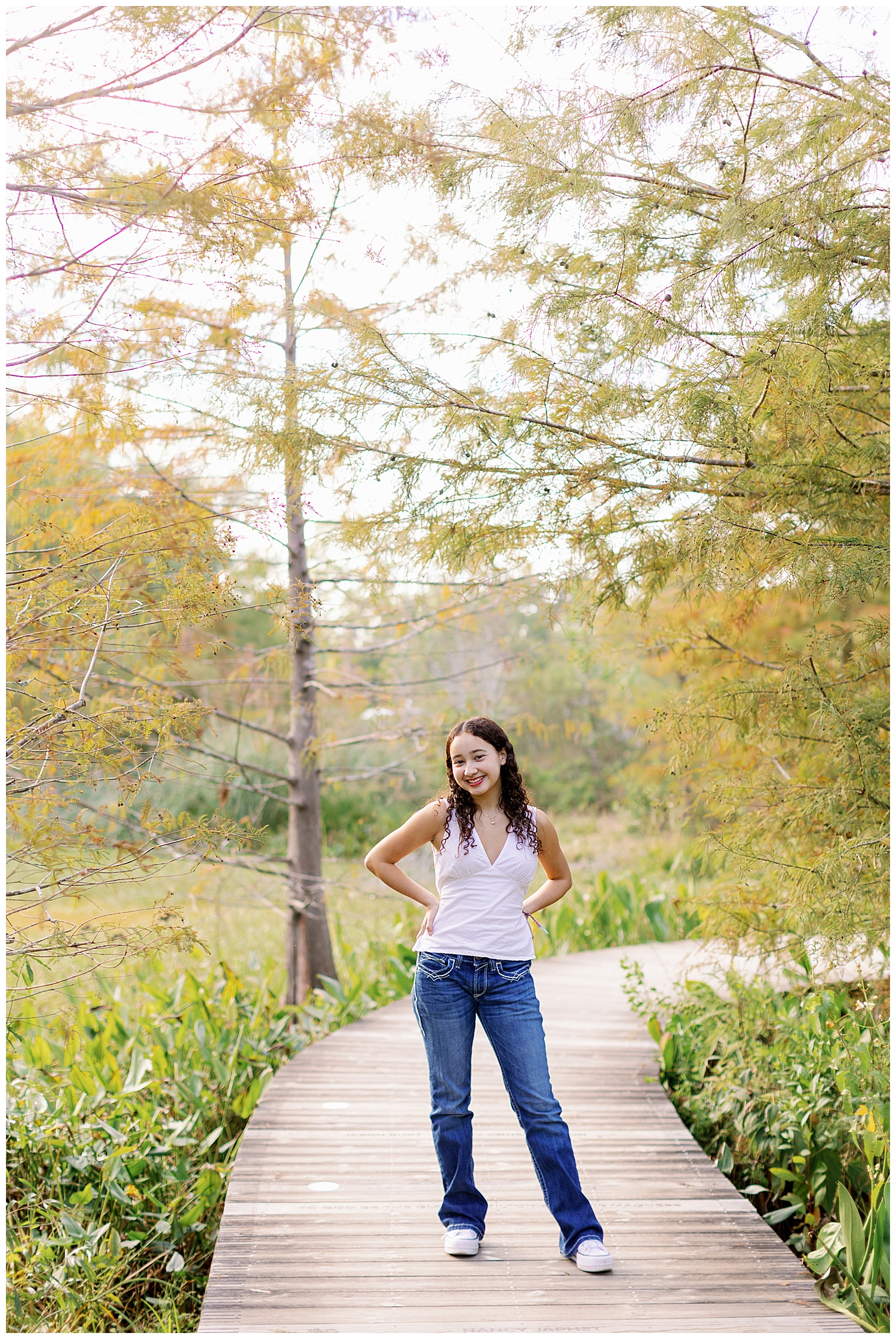 Houston senior girl in white shirt and jeans with hands on hip standing outside at Arboretum