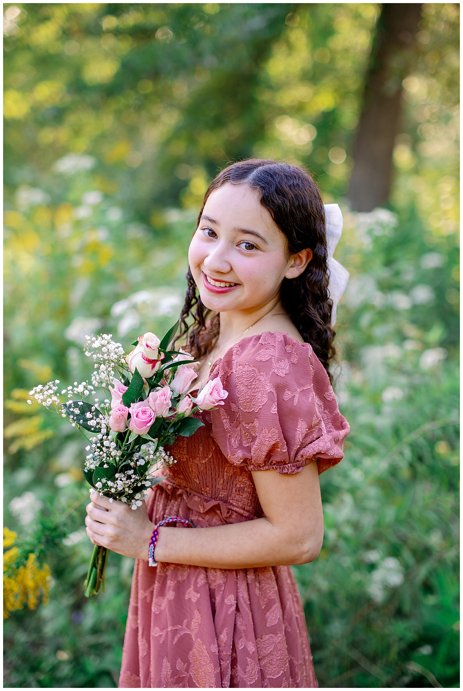 high school senior girl in mauve sundress holding flowers in a field