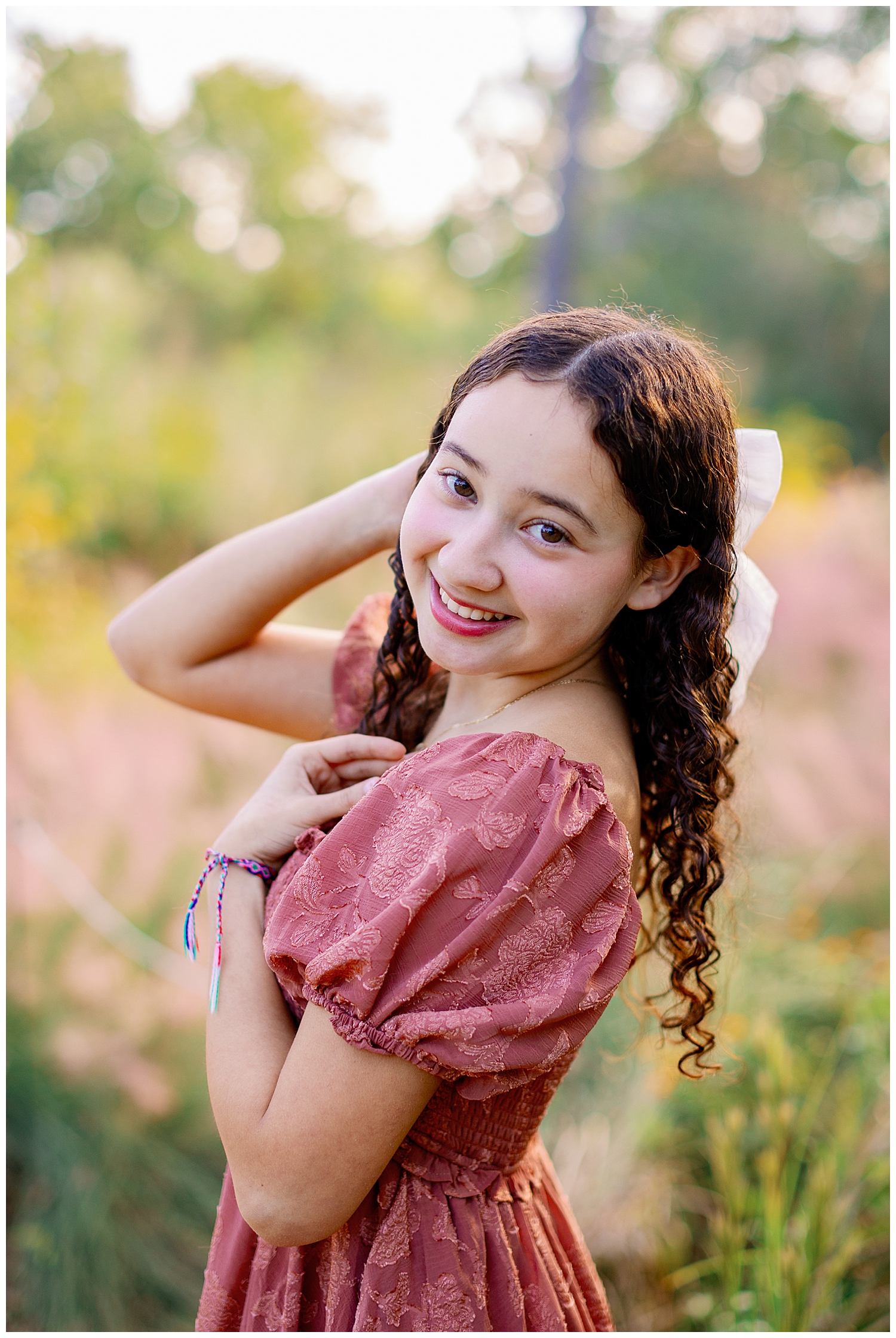 high school senior girl in blush dress and white bow standing in front of field at Houston Arboretum