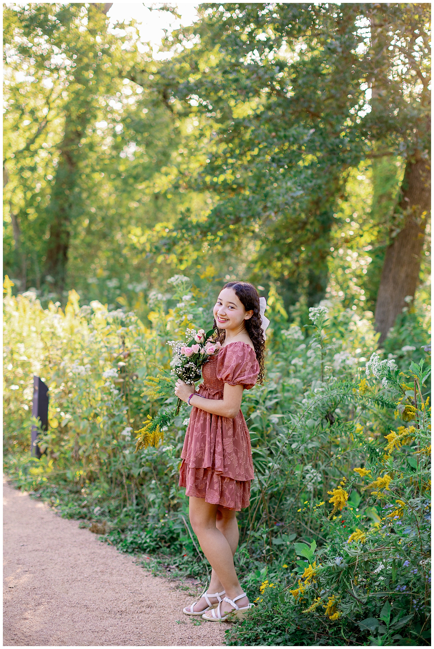 girl in pink sundress holding floral bouquet for Houston senior pictures with flowers at Arboretum