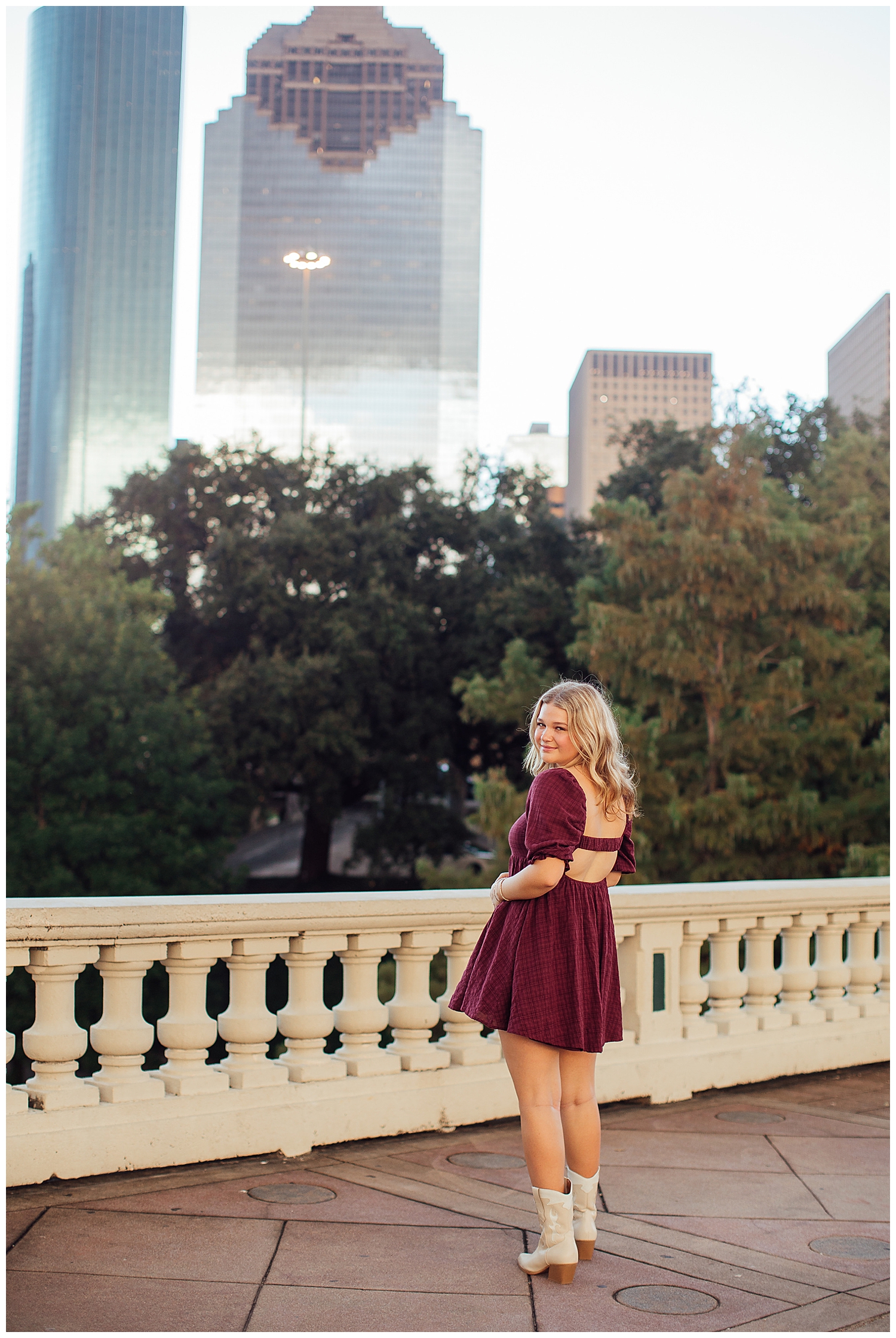 high school senior girl standing in front of Houston skyline maroon dress