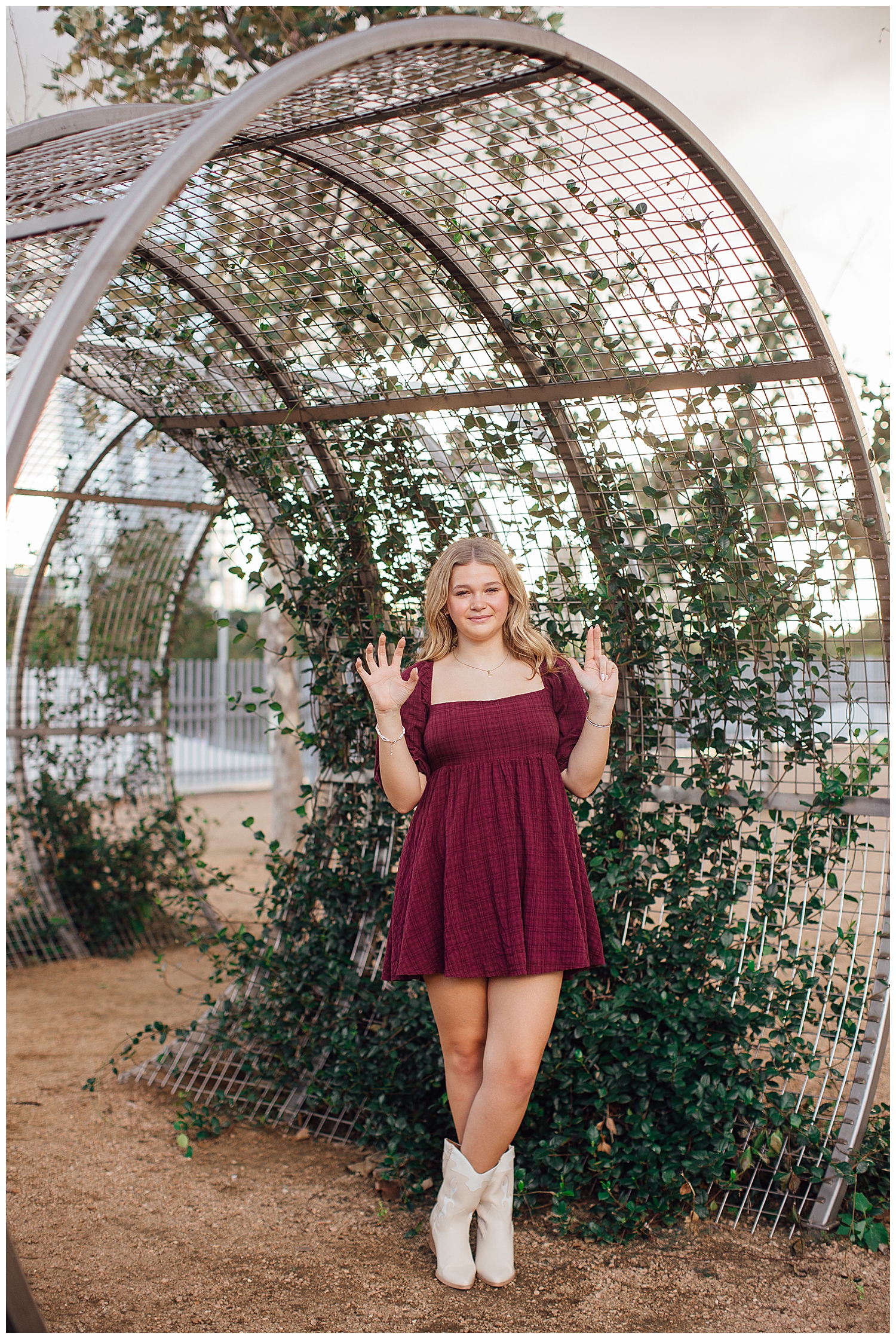high school senior girl standing outdoors in front of ivy arch downtown Houston in maroon dress
