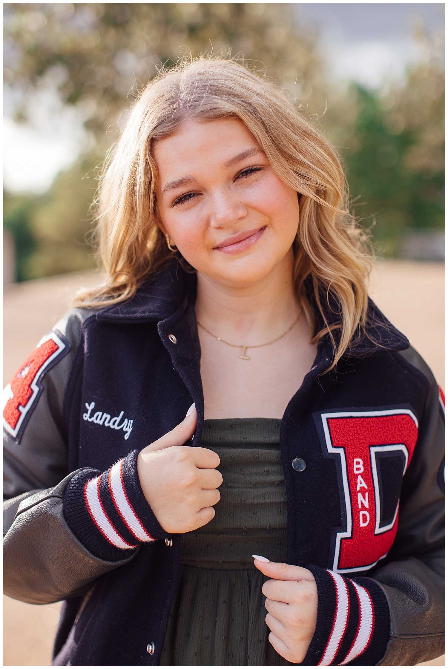 girl wearing navy and red letter jacket outdoors Houston and smiling