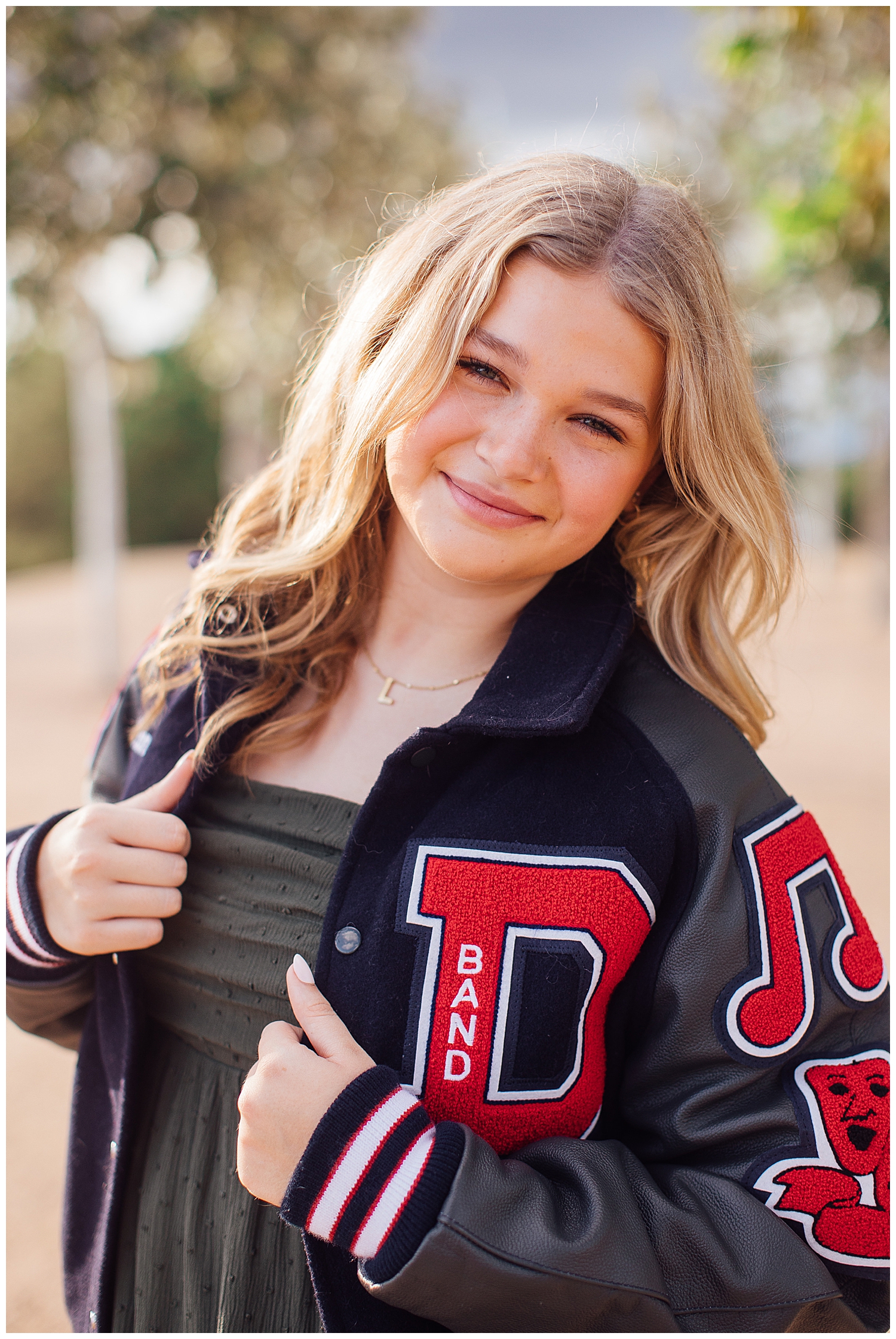 high school senior girl smiling and leaning in with hands on red and navy letterman jacket for Houston skyline senior pictures