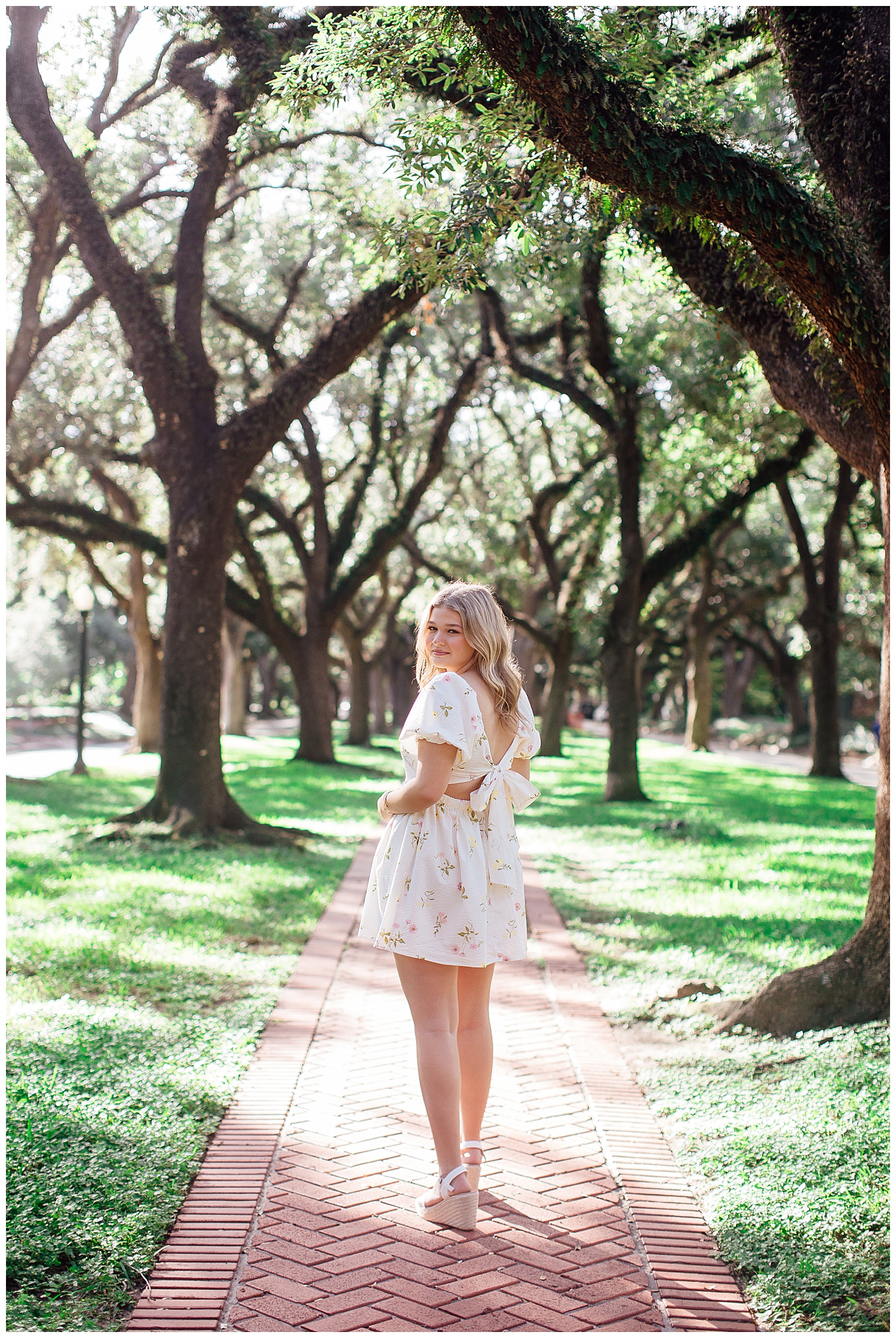 high school senior girl in white floral dress standing between trees outdoors Houston