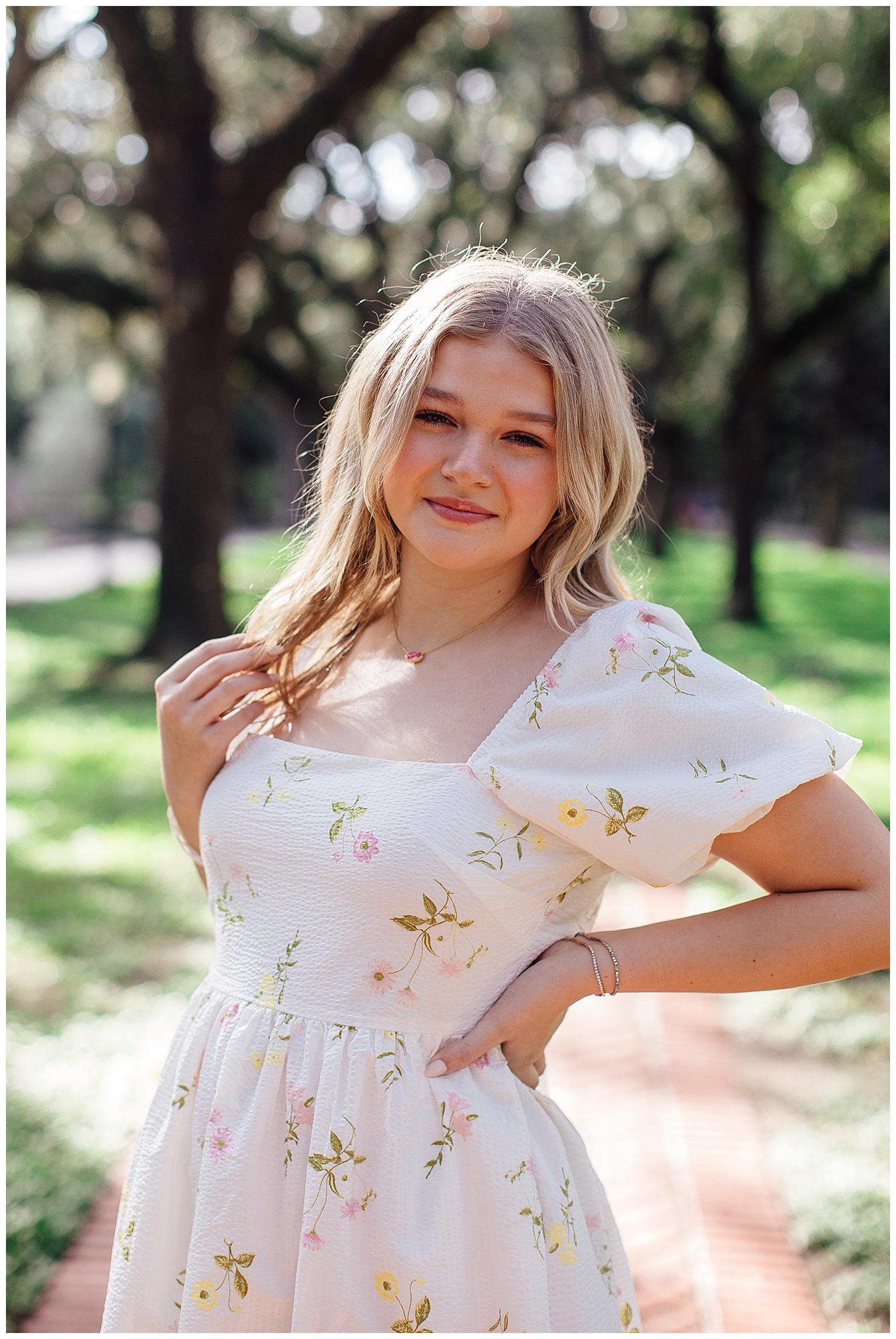girl in white floral sundress with hand in hair standing outside by trees Houston