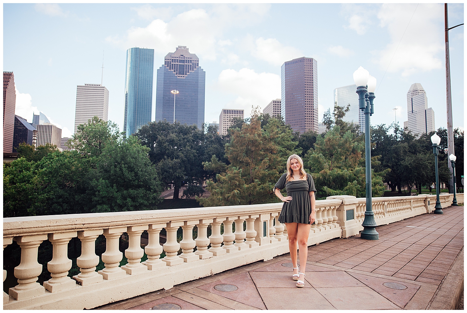 Houston skyline senior pictures with girl in army green dress and hand on hip standing Sabine Street Bridge