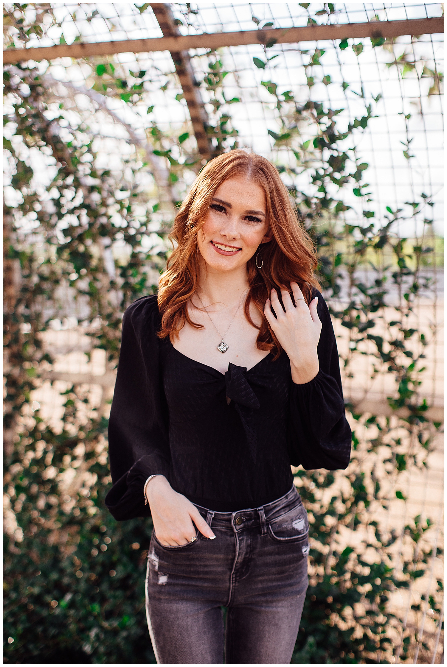 Houston senior girl with red hair wearing black shirt with hand in hair in front of ivy arch outdoors