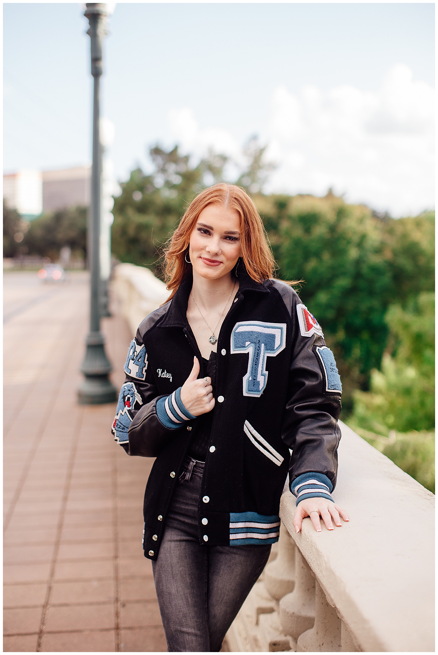 Outdoor Houston senior pictures with girl with red hair wearing navy letter jacket on Sabine Bridge