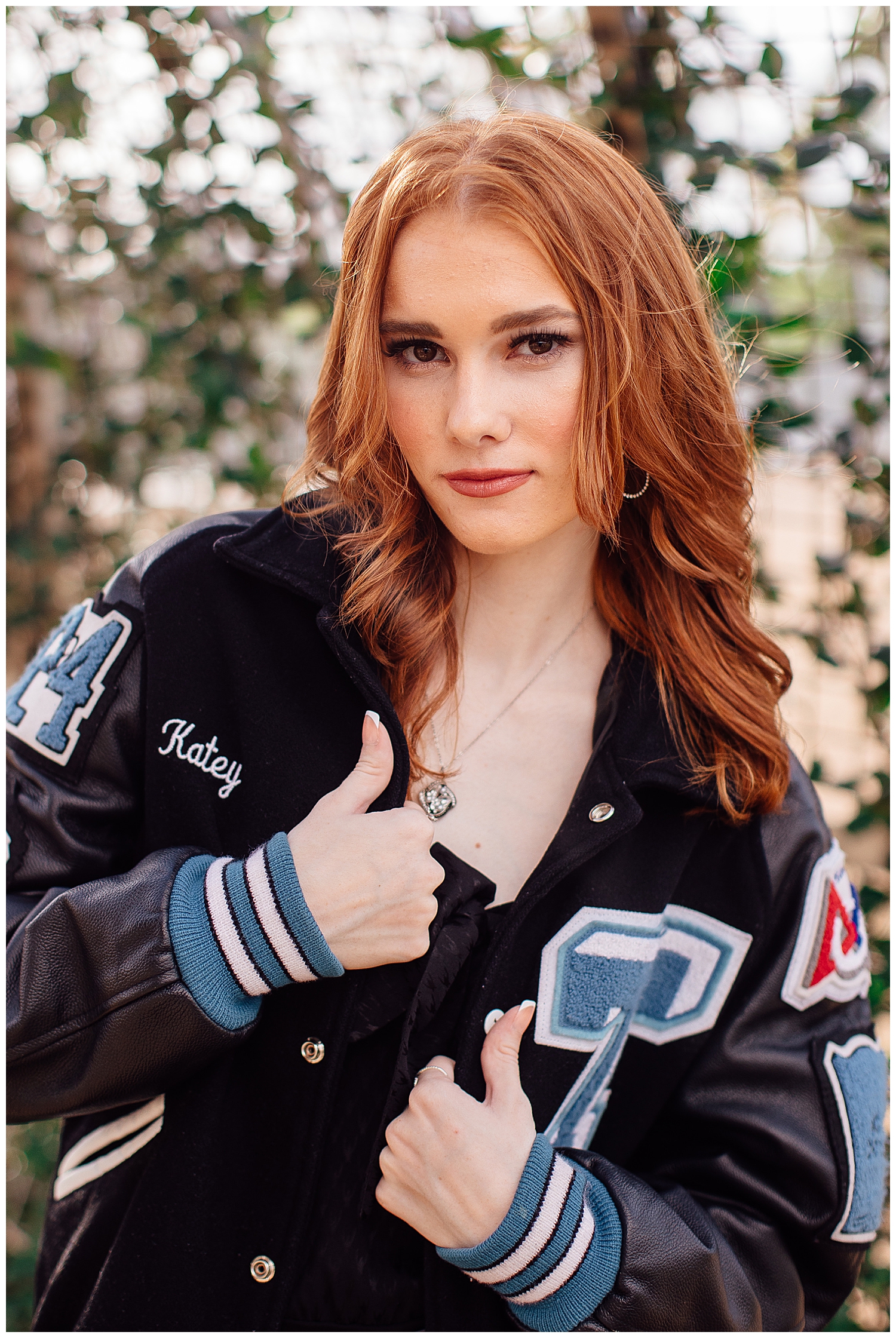 high school senior girl wearing letter jacket standing in front of ivy wall outdoor Houston senior pictures