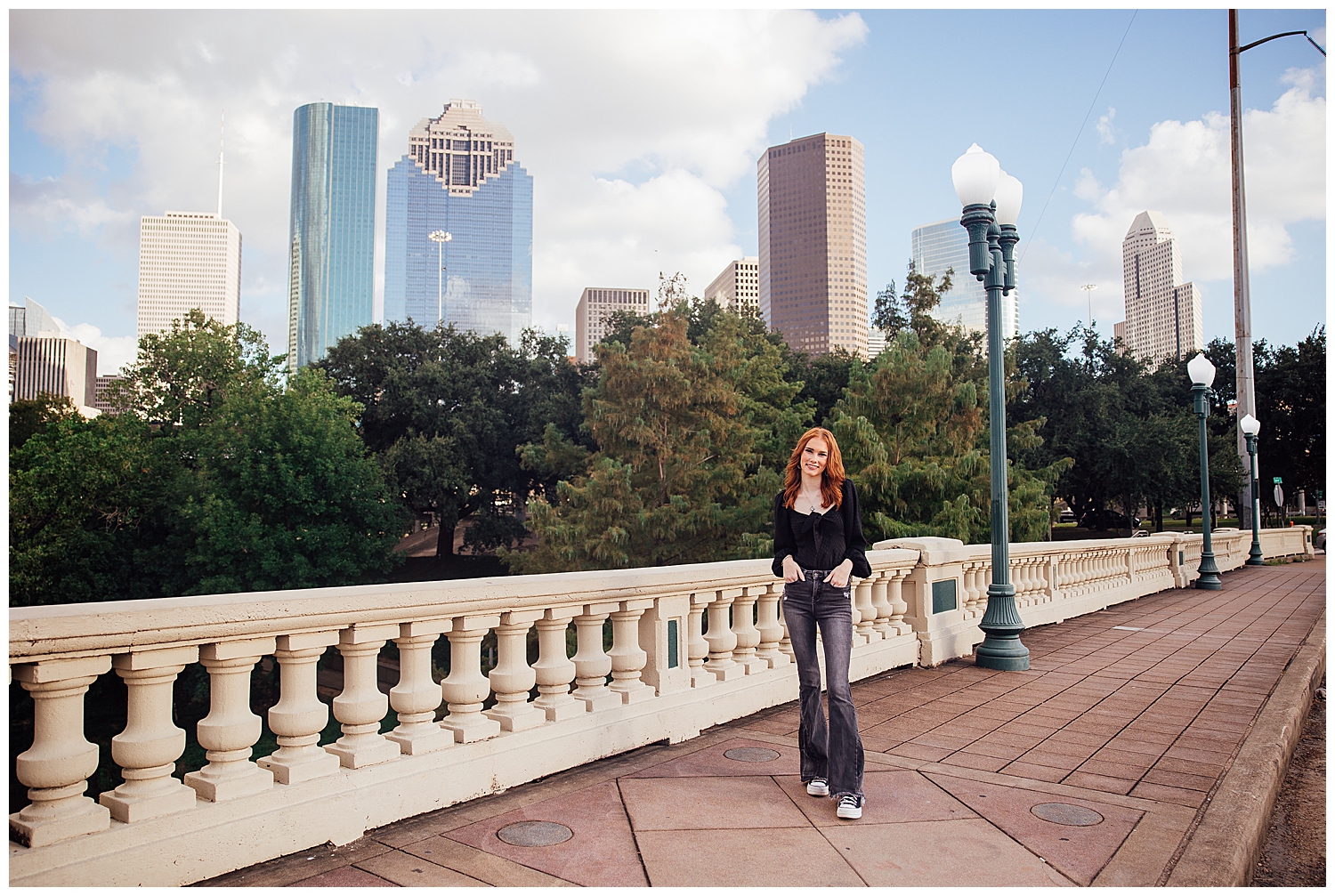 high school senior in black jeans and shirt standing in front of Houston skyline on Sabine Bridge