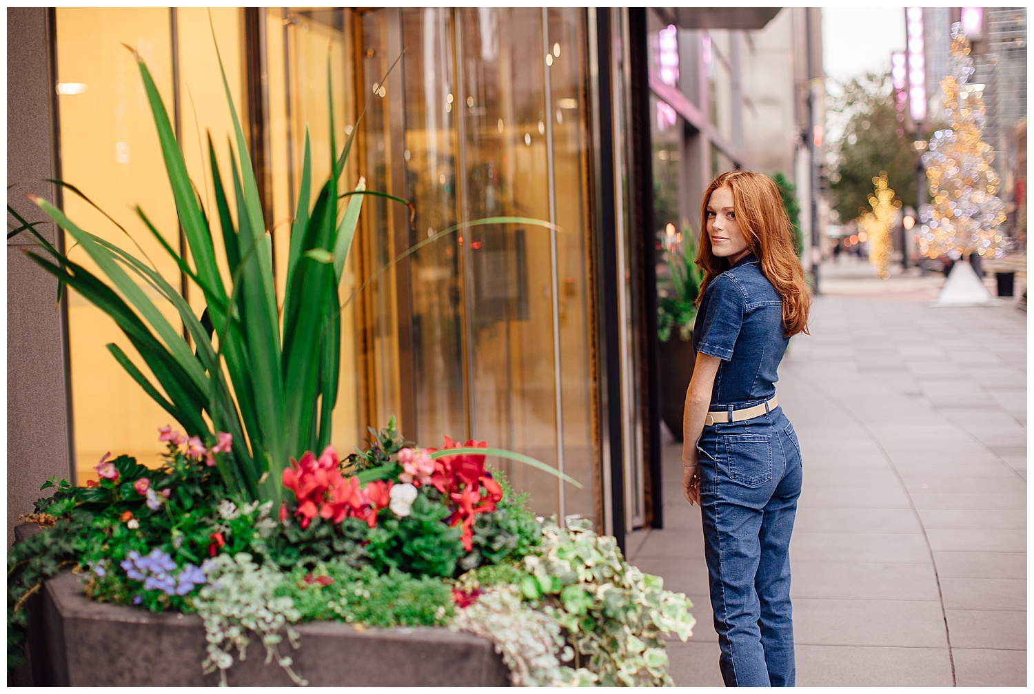 girl with red hair in denim jumpsuit standing in front of downtown Houston building with greenery