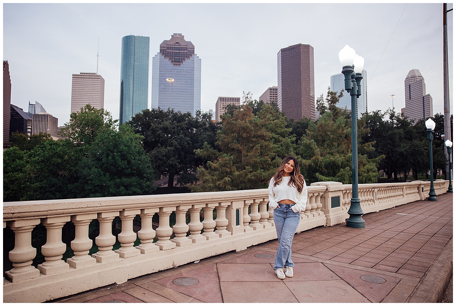 girl in denim jeans and white sweater standing in front of skyline downtown Houston senior photography session