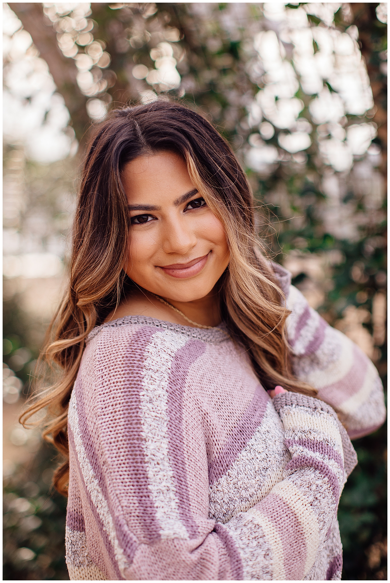 closeup image of high school senior girl smiling with hand in hair wearing purple white striped sweater outdoors Houston