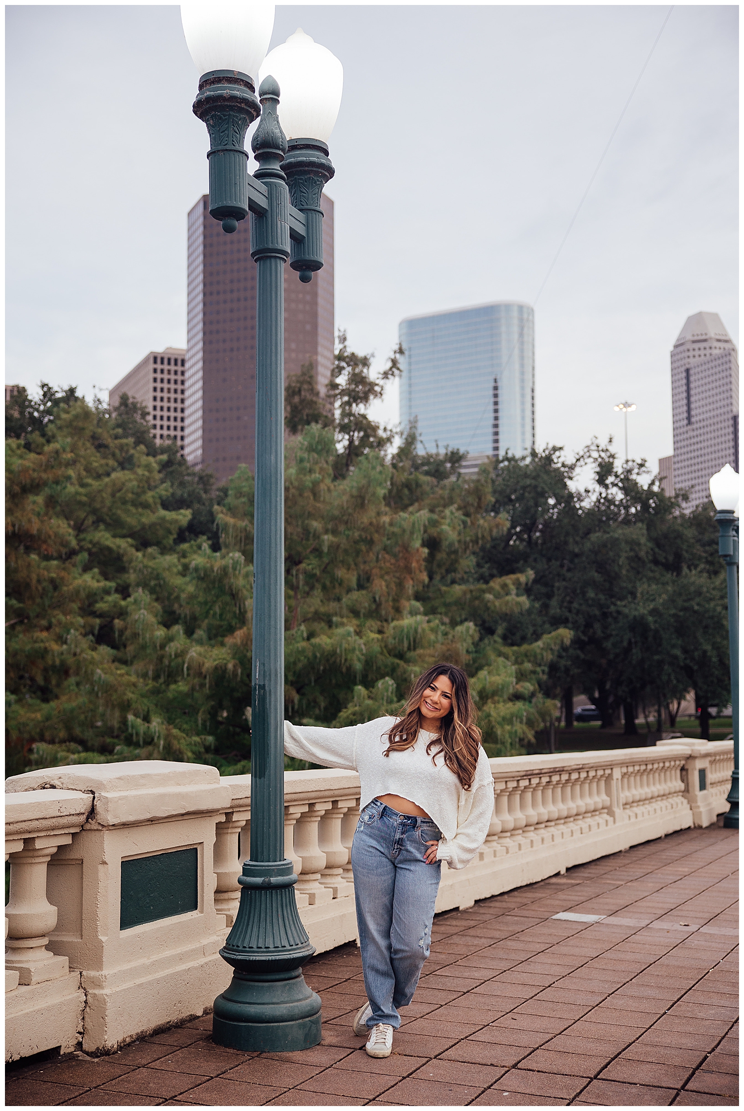 Houston senior photography session Sabine street bridge with girl in white shirt and jeans hanging off lamppost