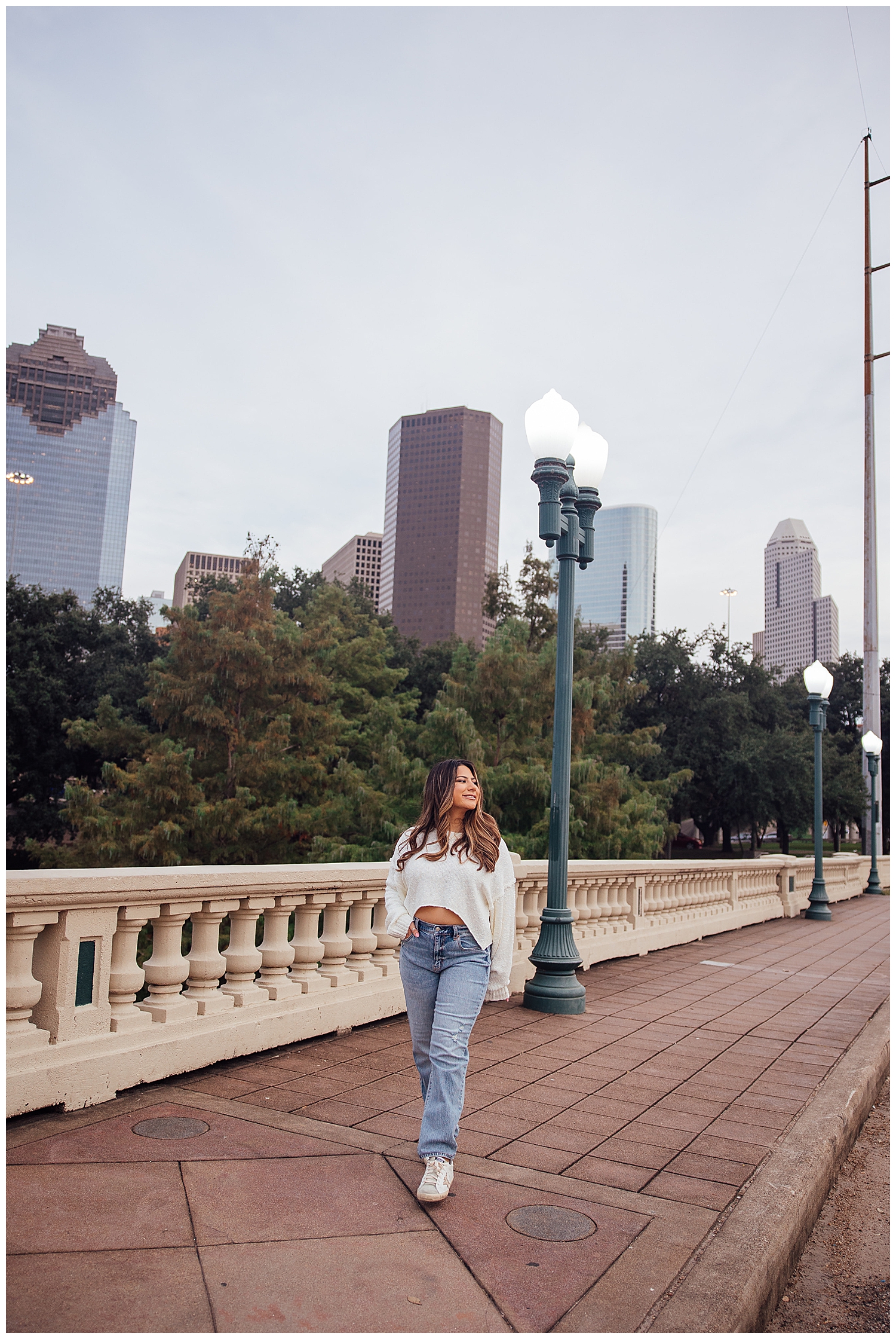Girl in jeans and white sweater walking on Sabine Street Bridge in front of Houston skyline
