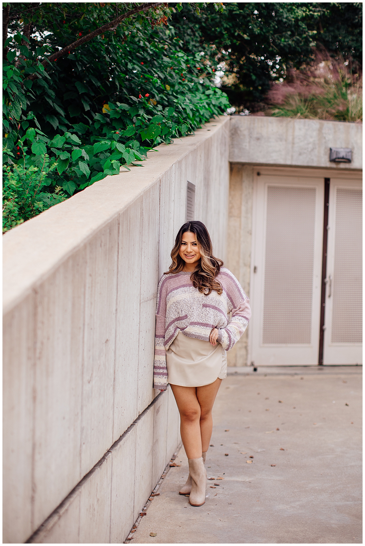 high school senior girl in white skirt and purple white sweater leaning against white wall Sabine Park