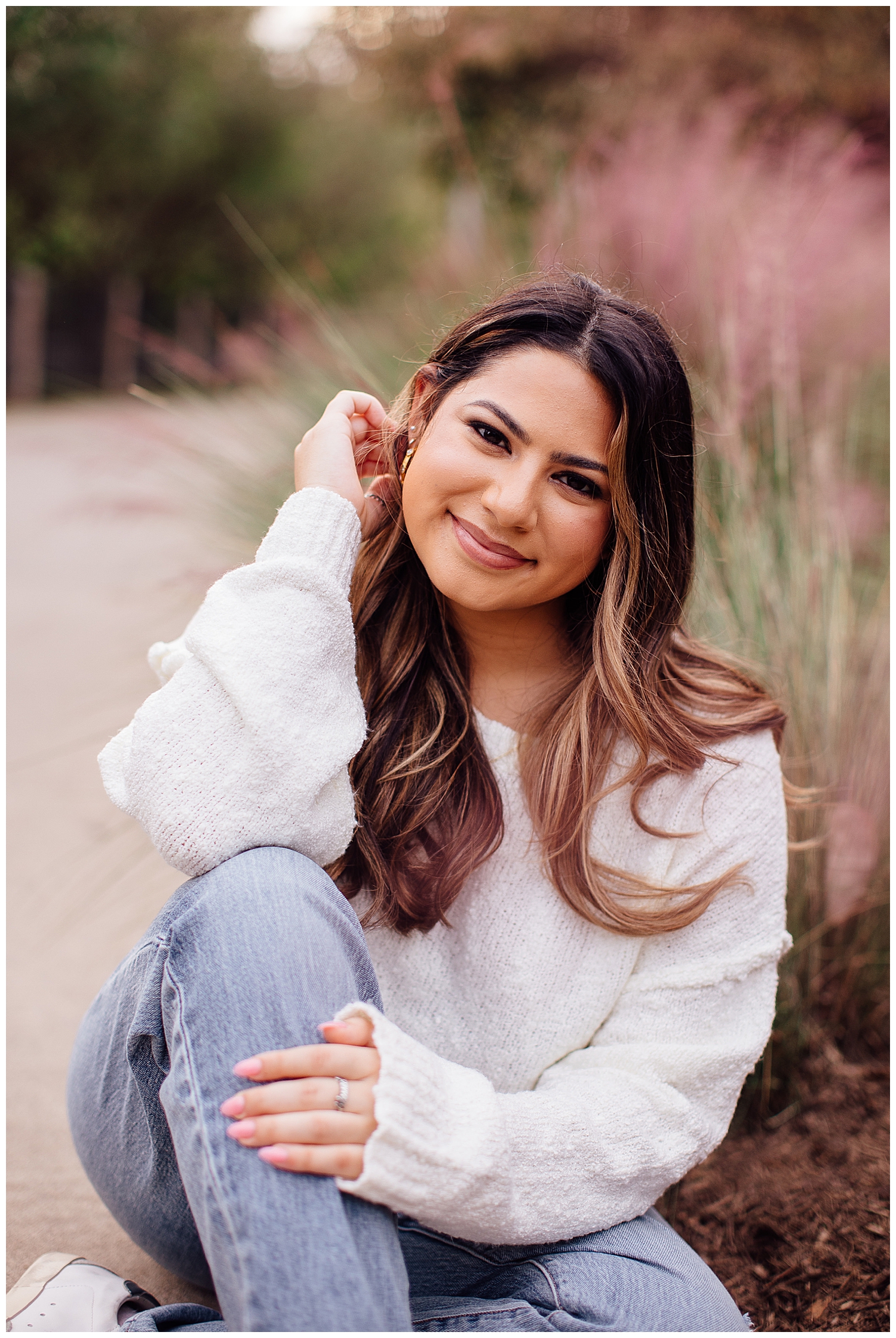 closeup image of high school senior girl in jeans and white sweater sitting in Houston field