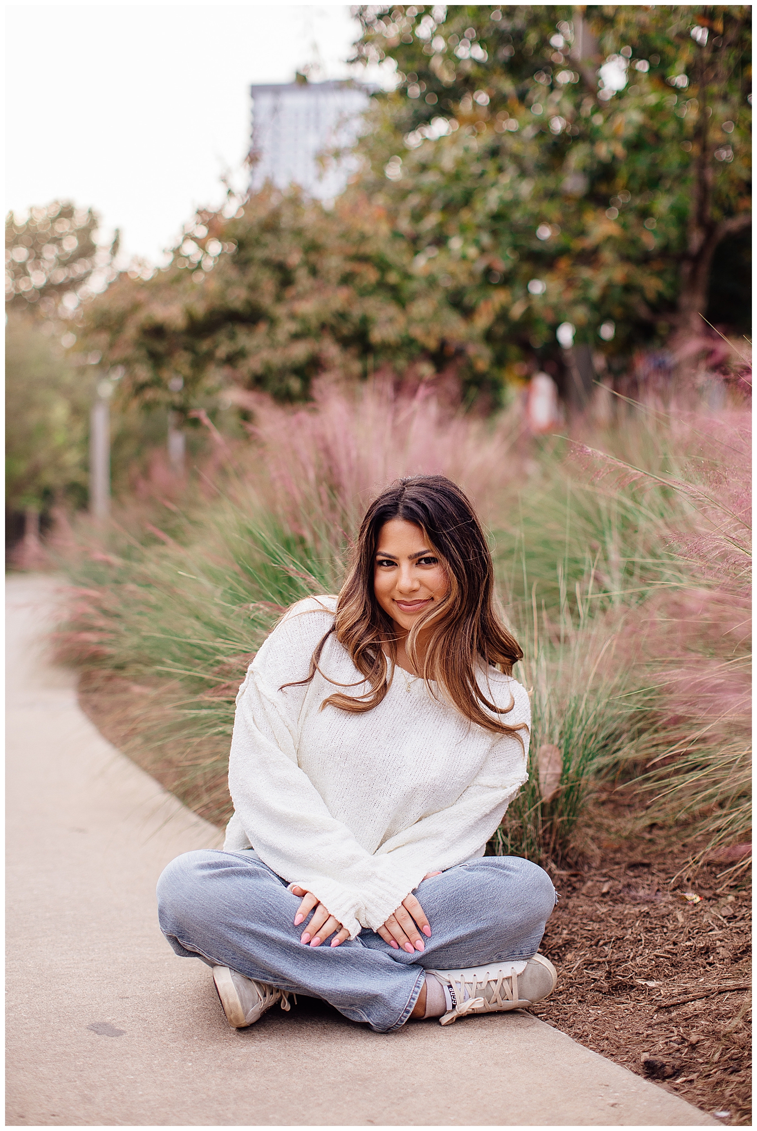 Houston senior photography sessions where girl is sitting on ground in jeans and white shirt smiling