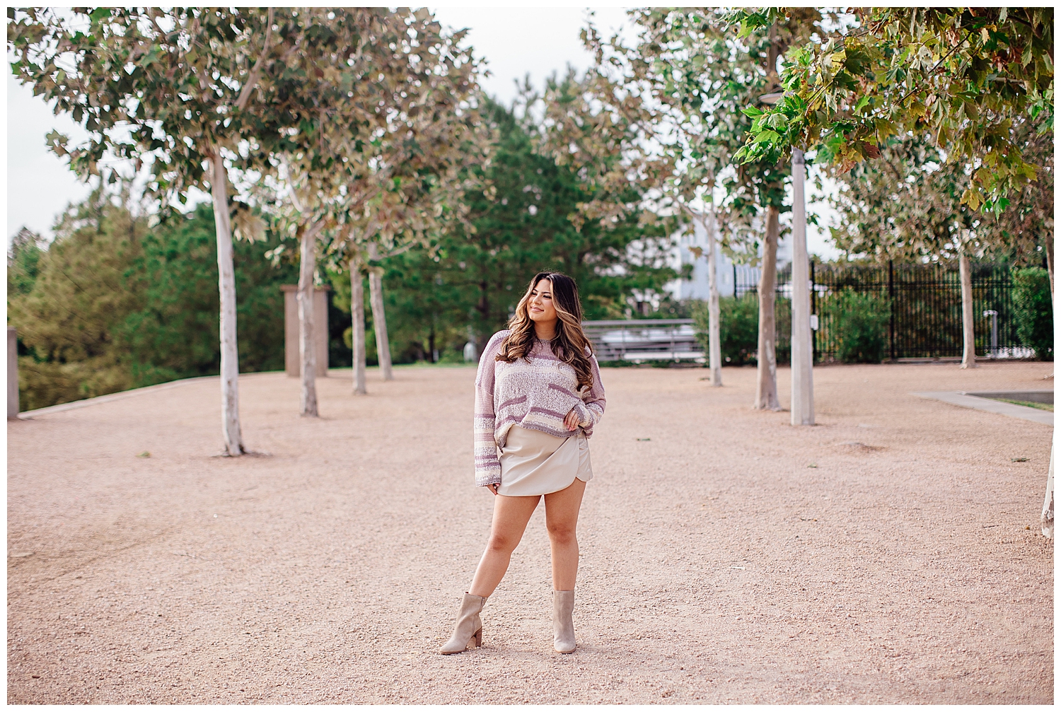 high school senior girl in white boots, white skirt and purple sweater standing outdoors between trees Houston