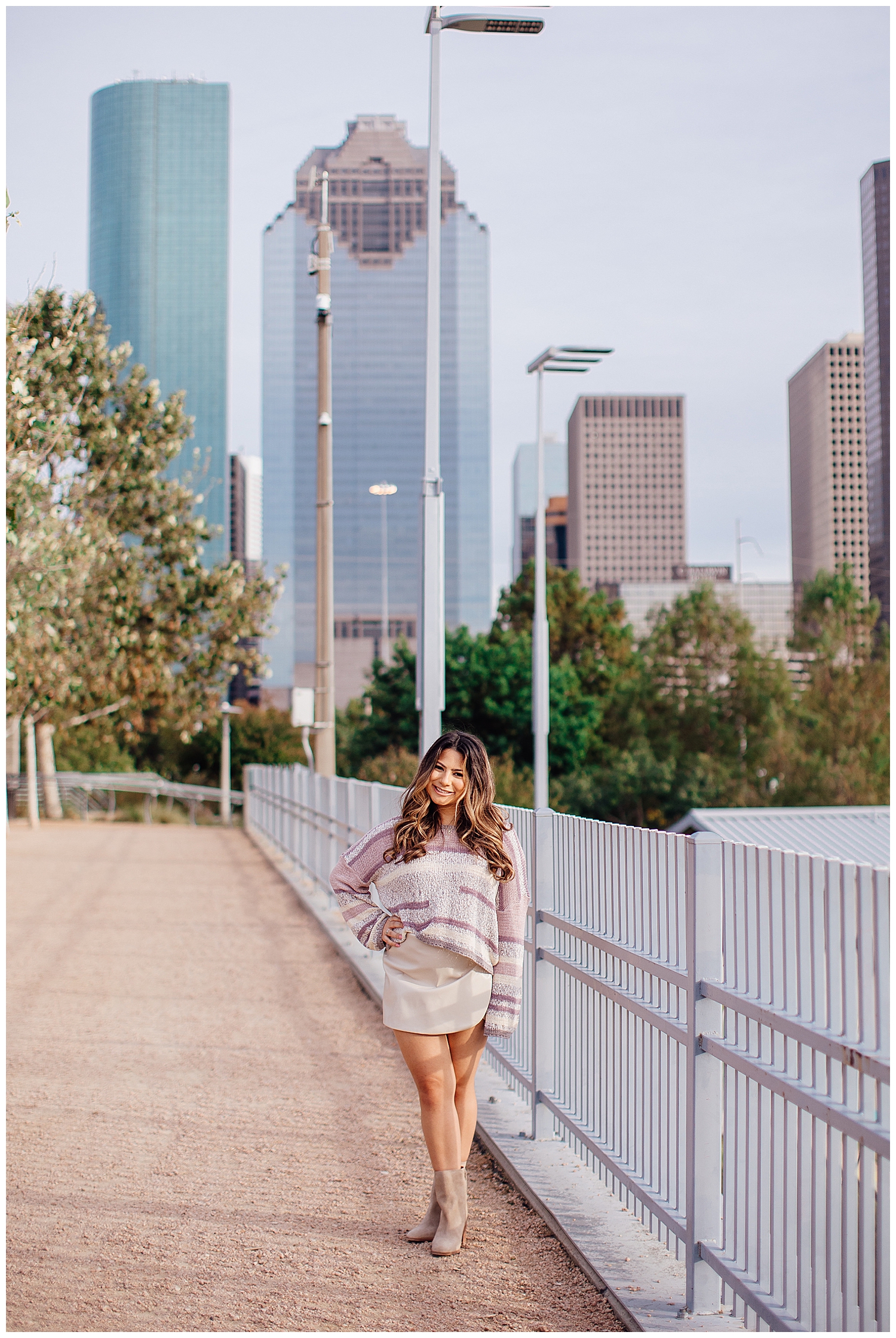 high school senior girl walking at Buffalo Bayou park in front of Houston skyline white skirt and sweater