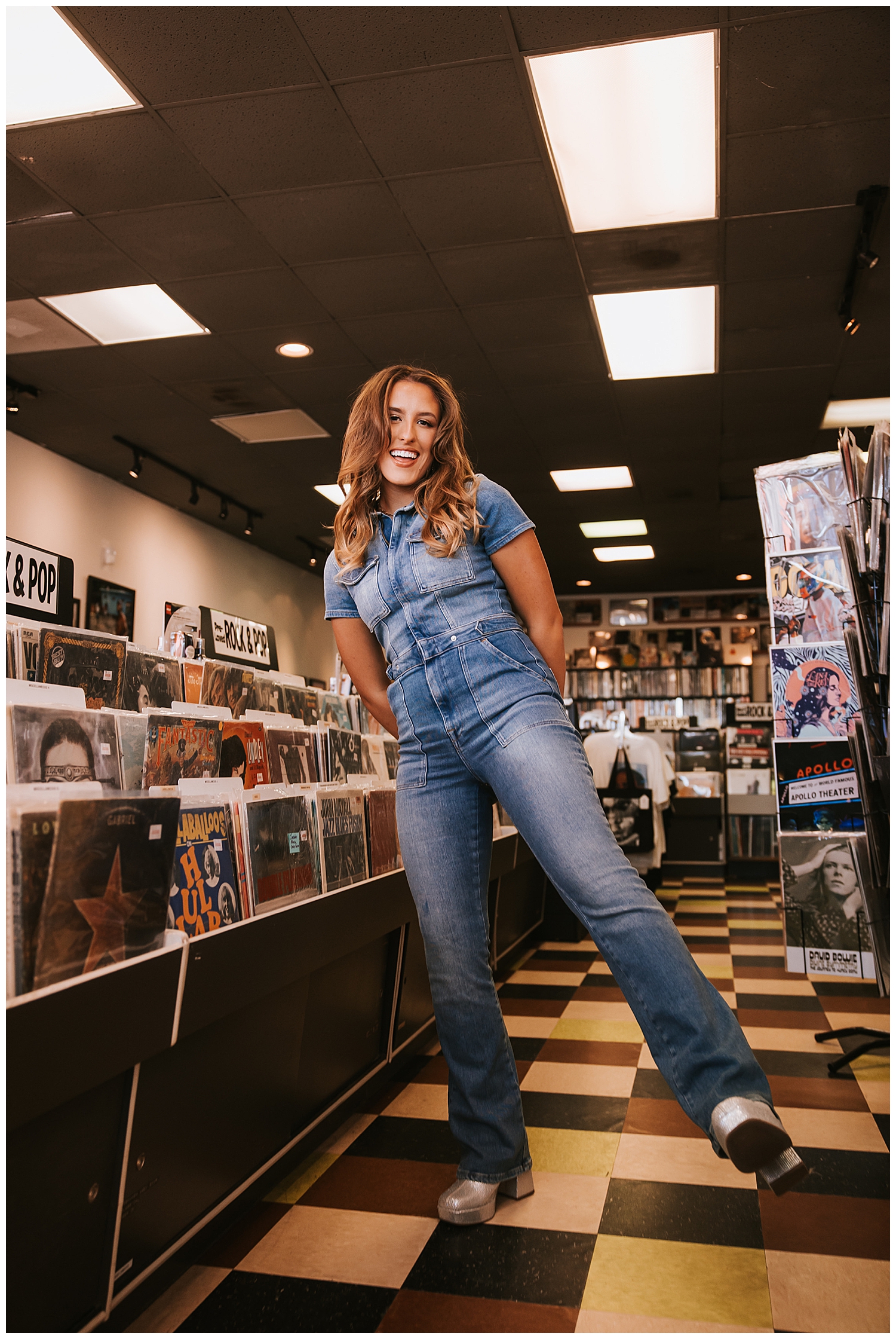 girl in denim jumpsuit standing inside a record store Houston and smiling