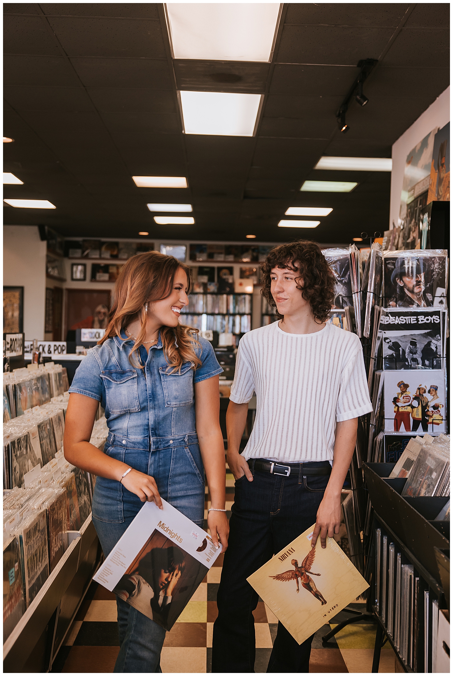 high school girl and boy siblings smiling at each other inside record store holding albums in hands