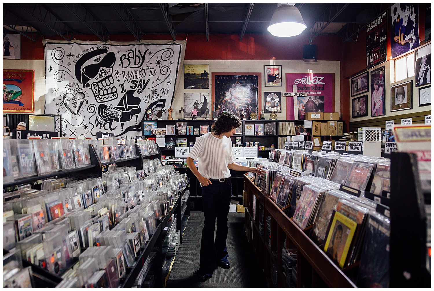 high school senior guy in black jeans, white tshirt looking at row of records inside Cactus Record store