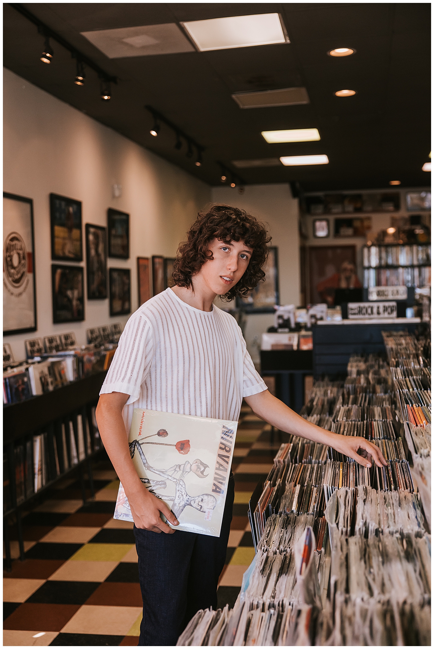 high school senior boy looking at record albums inside Cactus Recors wearing white shirt black jean