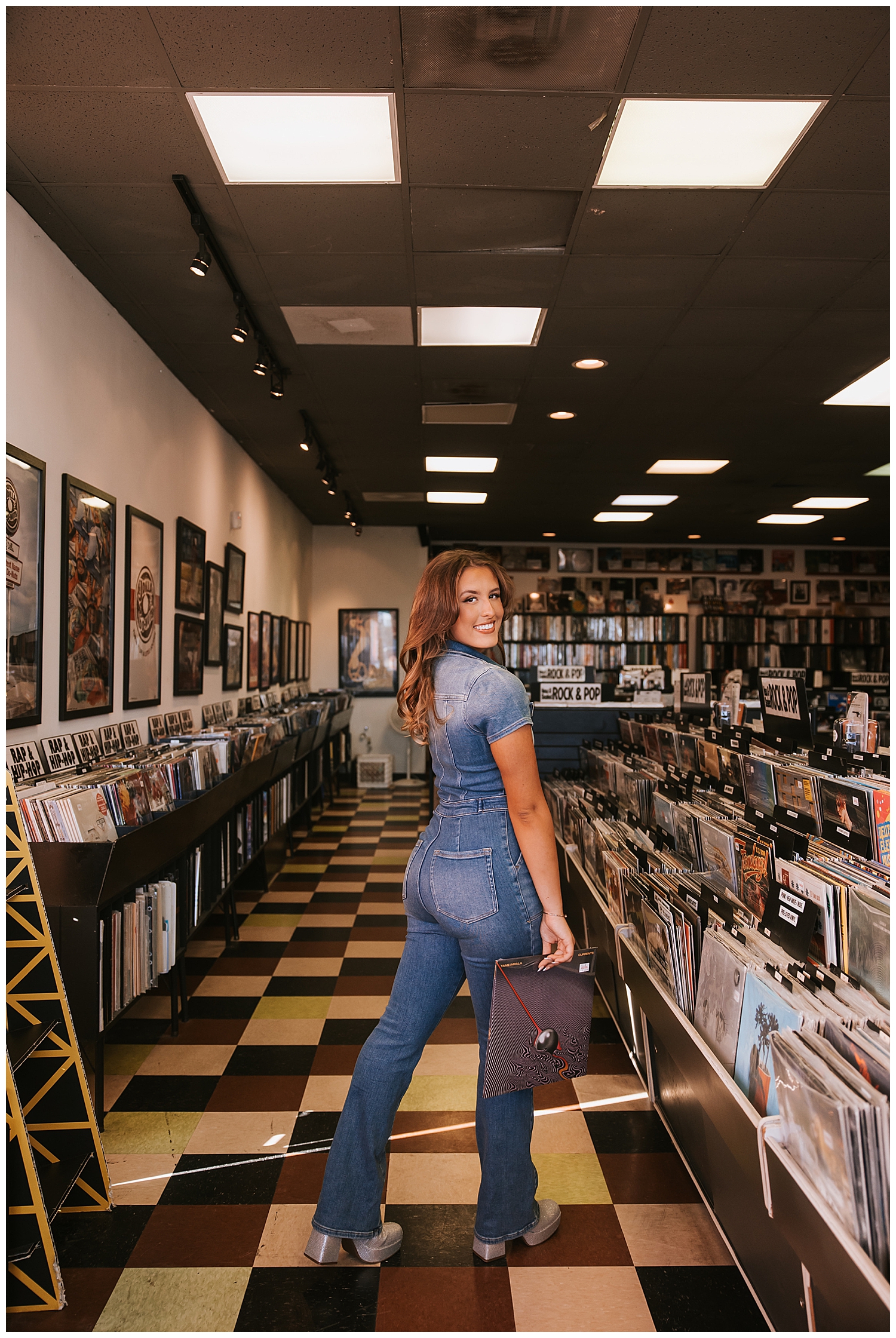 record store senior pictures with girl in denim jumpsuit holding album down by her side looking at camera