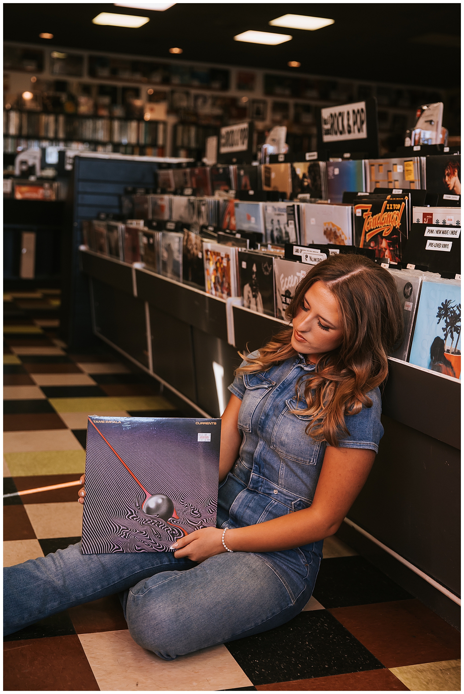 high school senior girl sitting on checkered floor holding record album inside Cactus Record store Houston