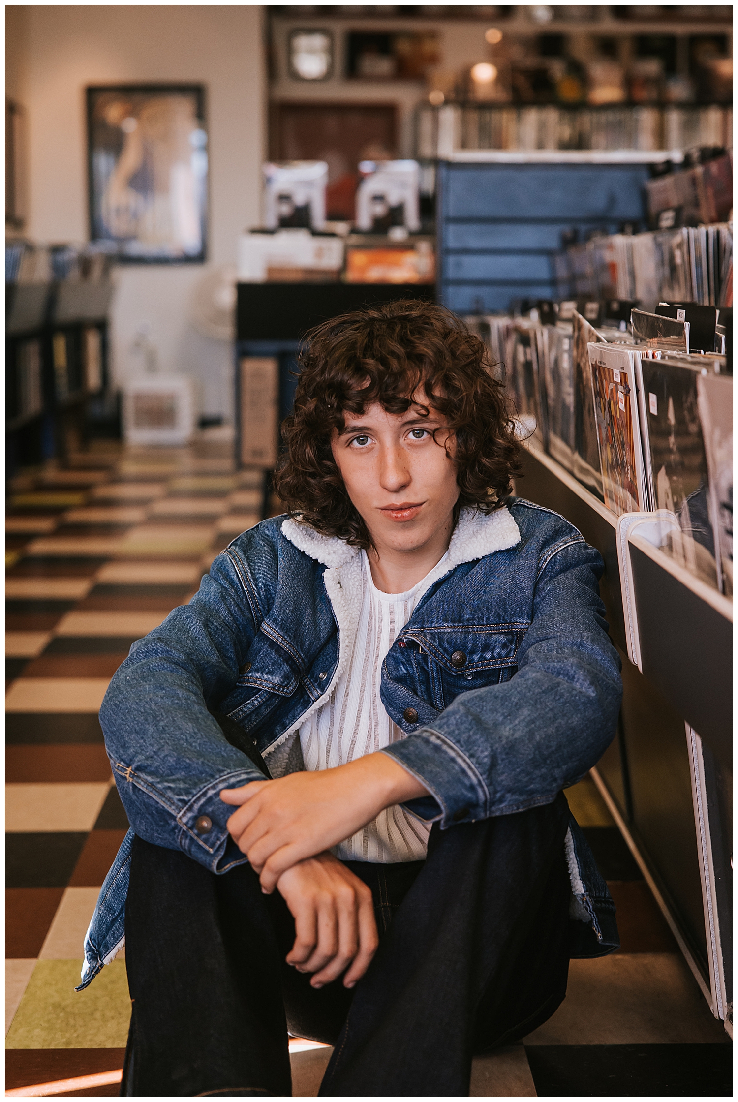 boy in denim jacket sitting on checkered floor inside a Houston record store