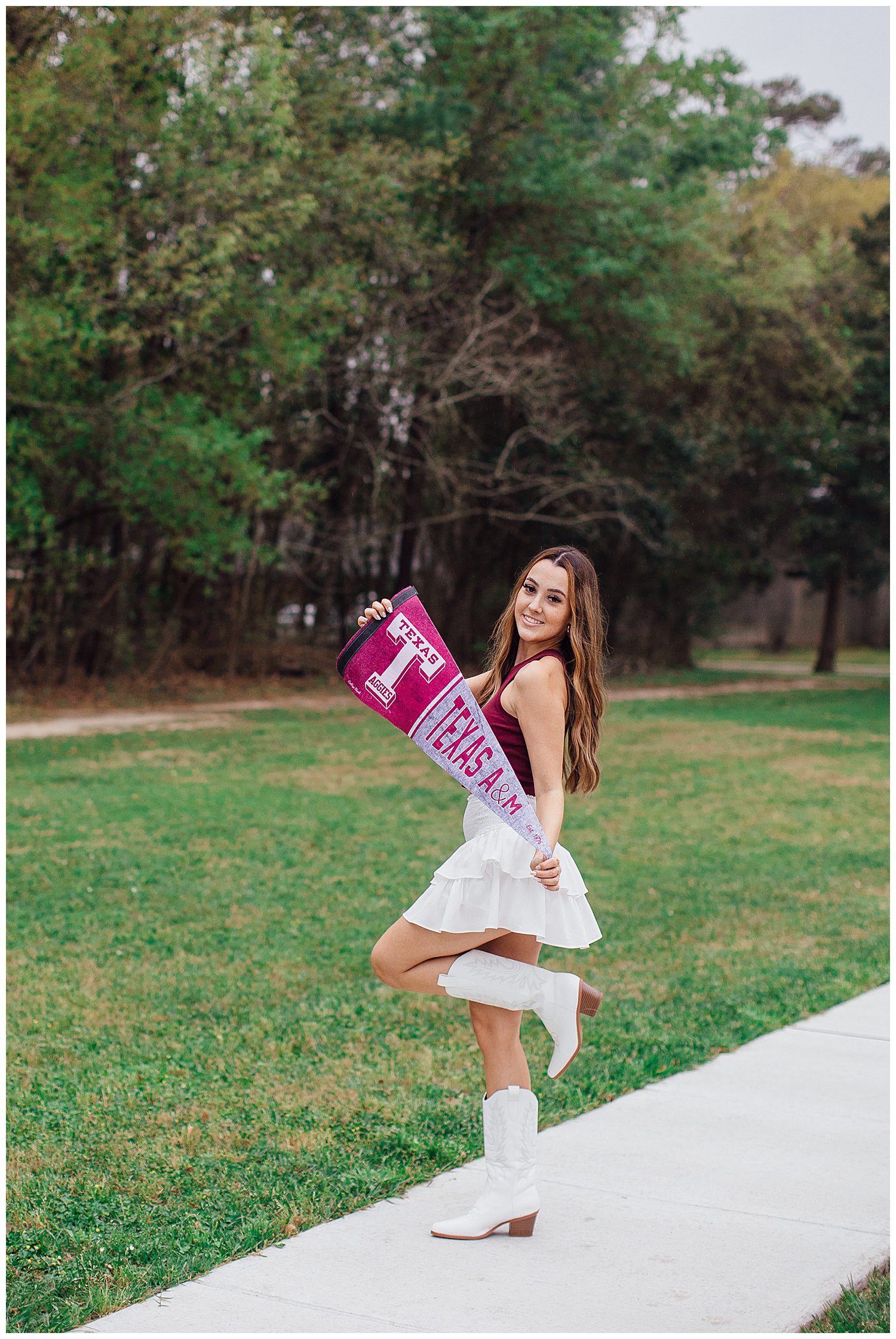 high school senior girl with white boots and skirt and maroon shirt holding Texas Aggie sign in a Houston field