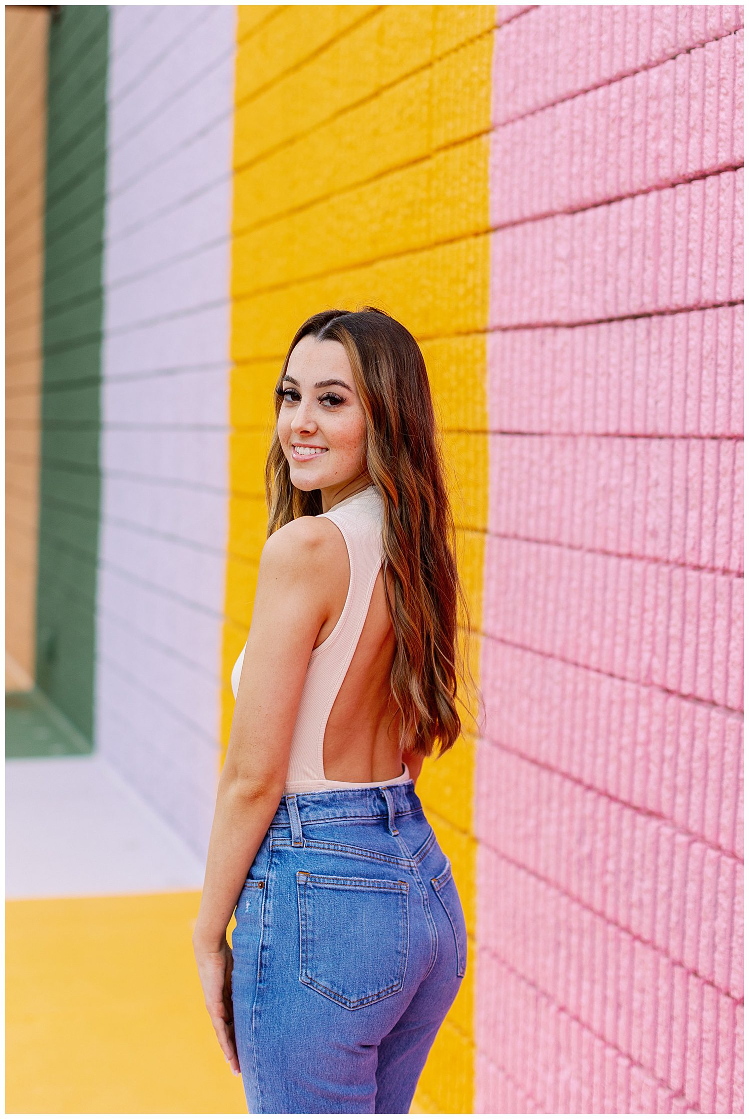 close up image of girl in beige shirt and jeans looking over her shoulder in front of yellow and pink Sugar and Cloth Color Wall portraits Houston