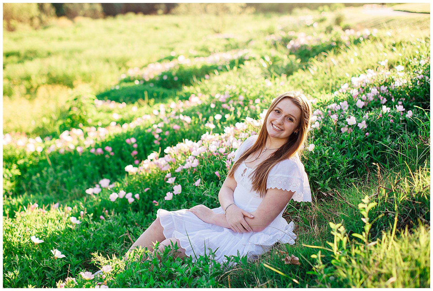 girl in white dress sitting in a field downtown Houston smiling with pink flowers