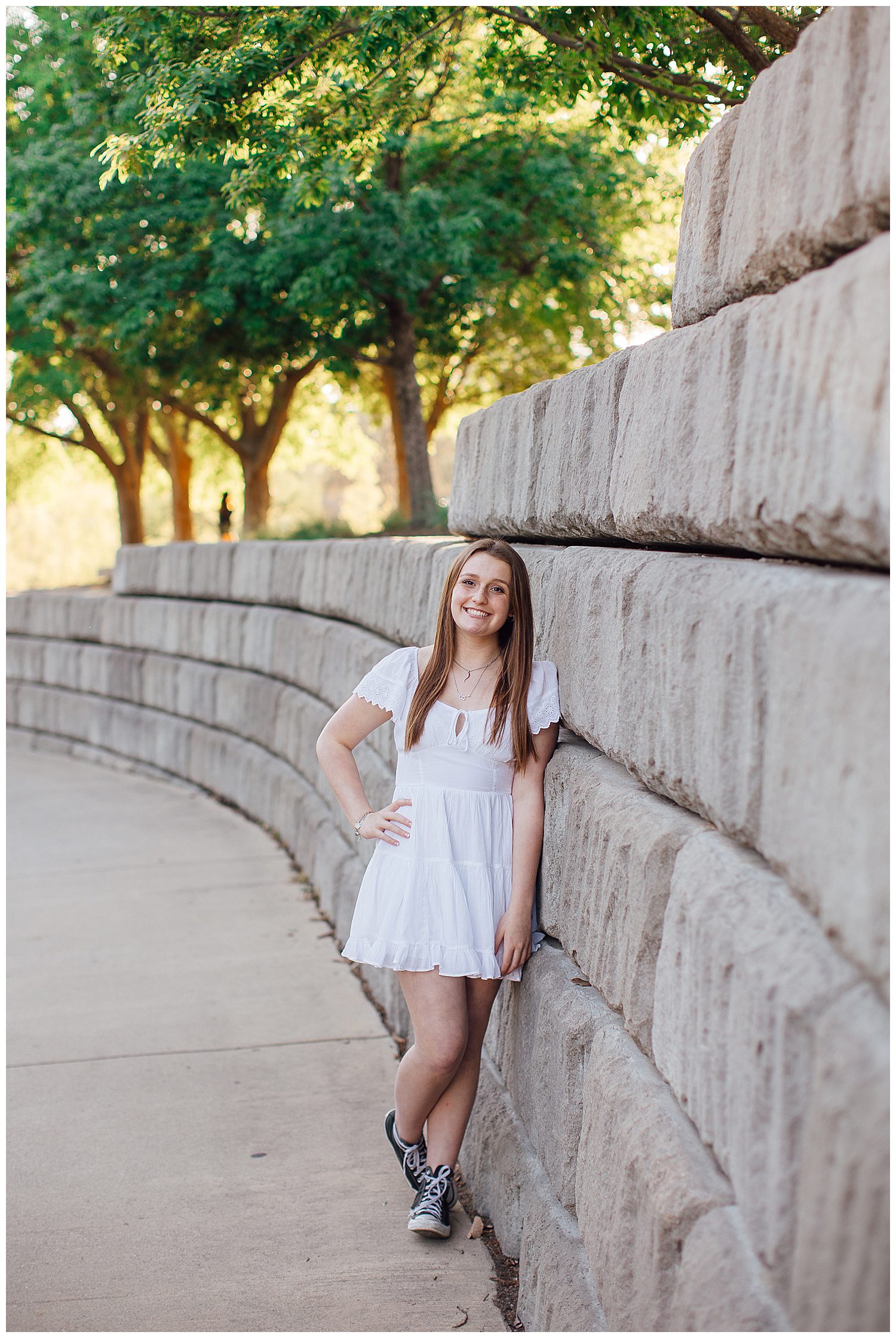 high school senior girl in white dress with black converse shoes leaning against wall for spring senior portraits Houston Sabine Park
