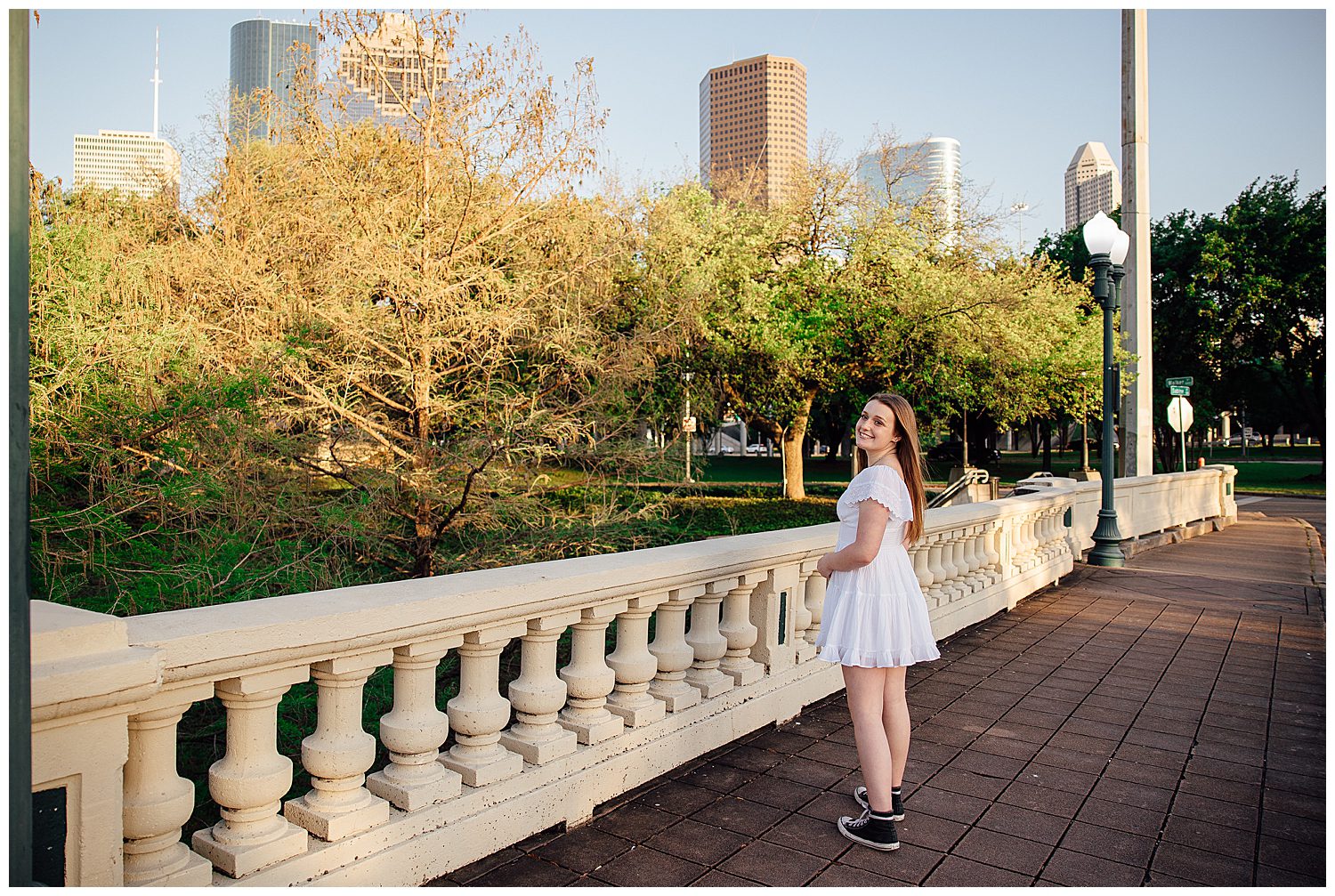 girl in white sundress look over her should for Spring Senior Portraits Houston on Sabine Street bridge in front of skyline