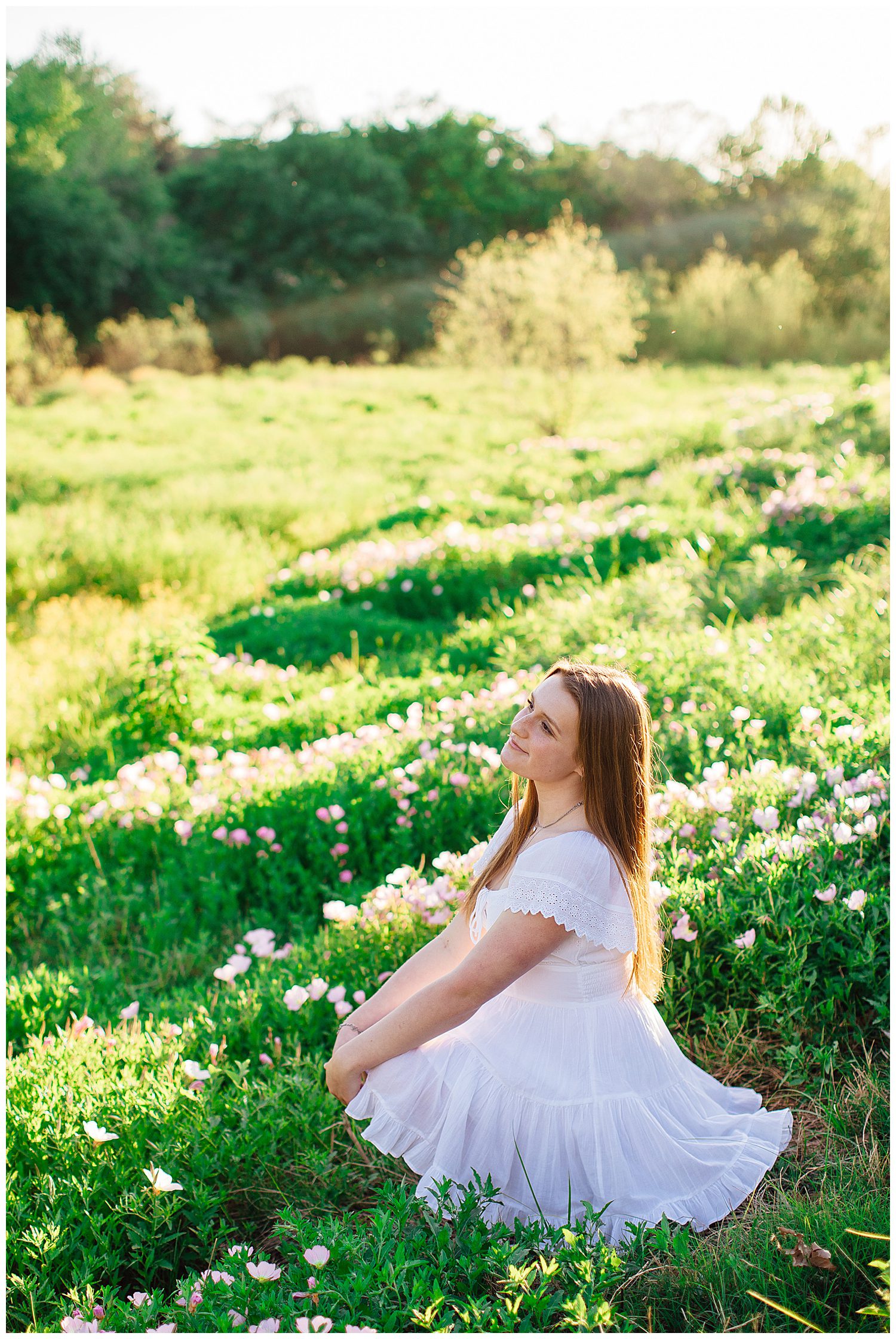 girl in white sundress sitting in a green field with pink flowers downtown Houston