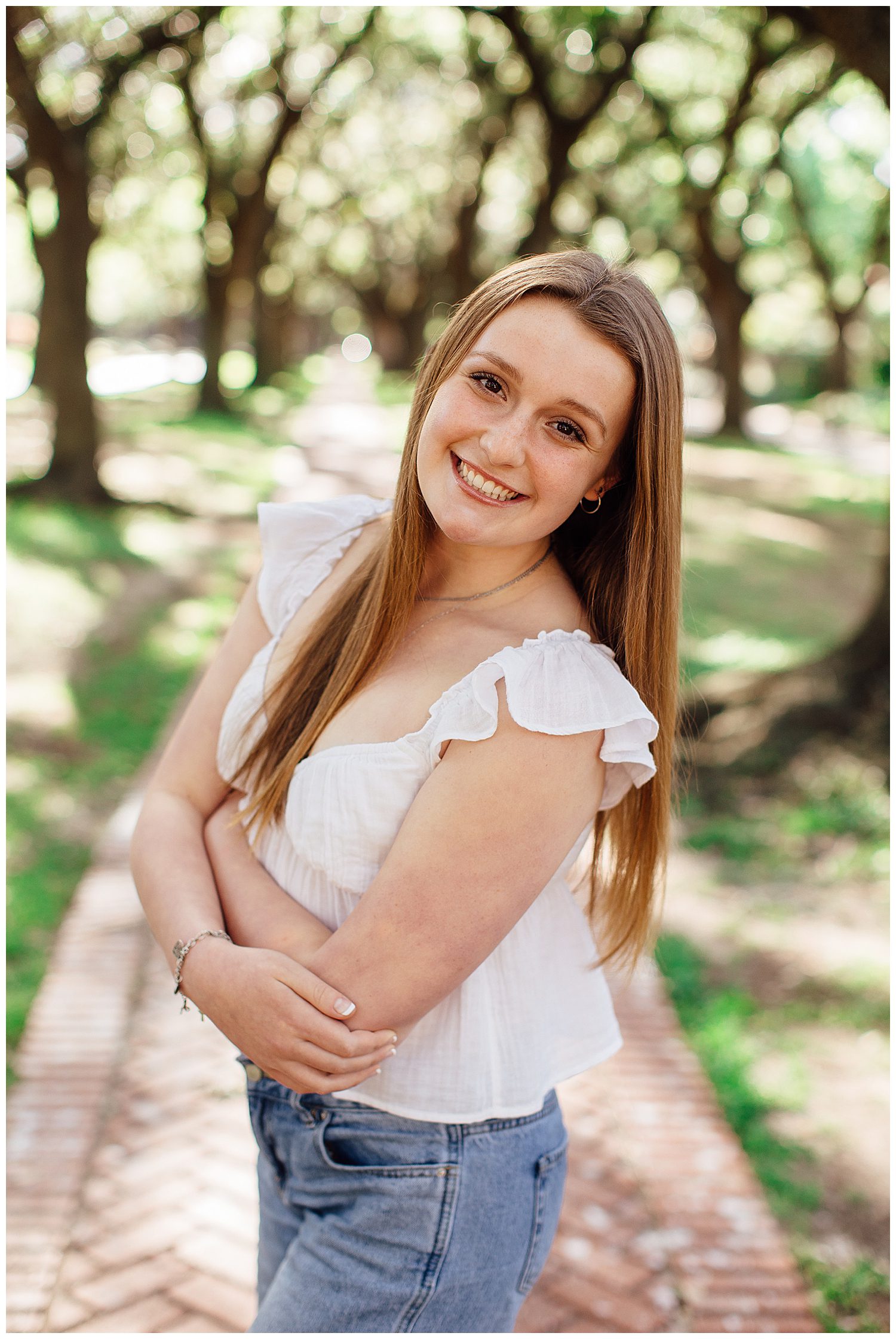 close up image of high school senior girl in jeans and white shirt smiling outdoors with hands crossed