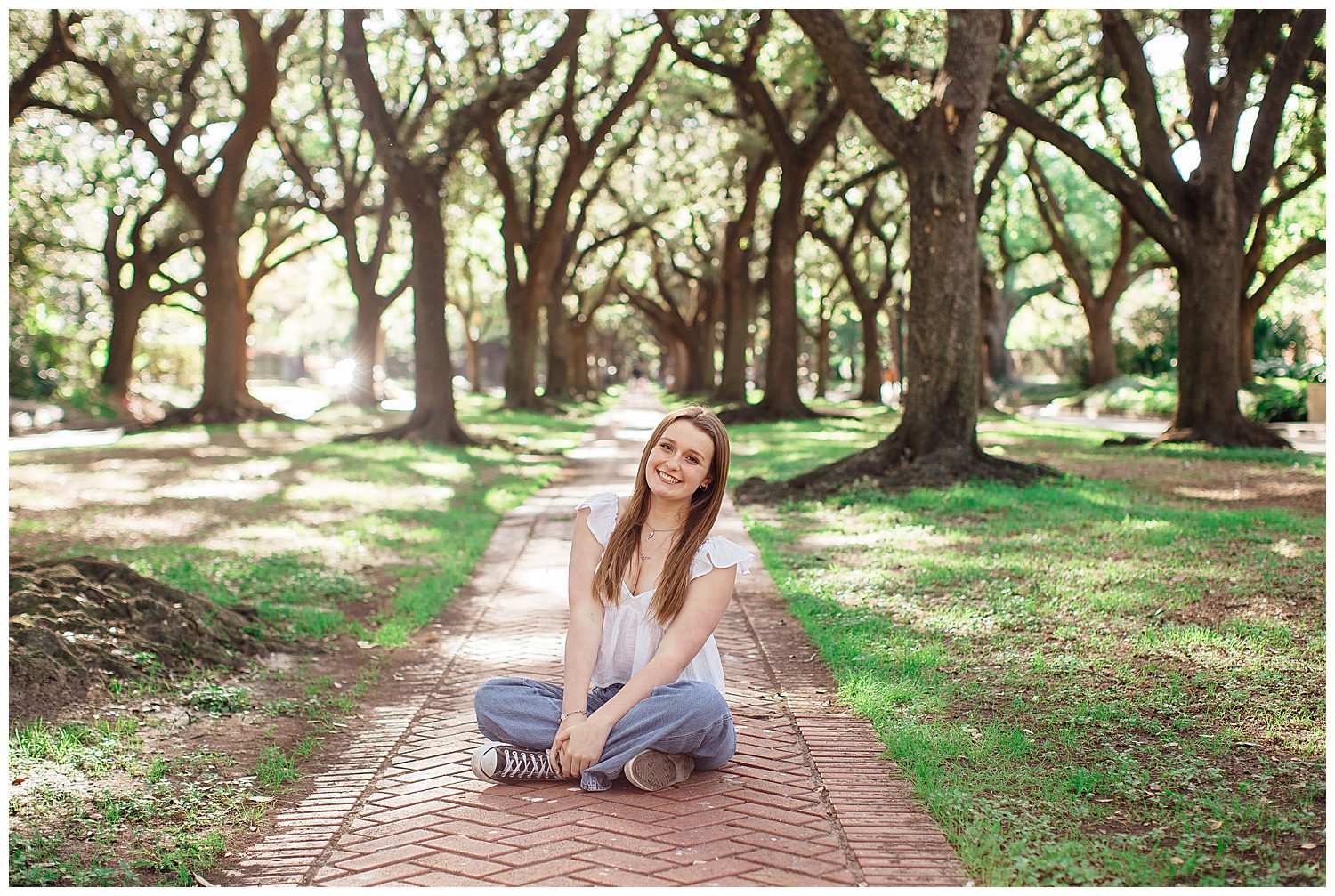 high school senior girl sitting on sidewalk between outdoor Houston tree line