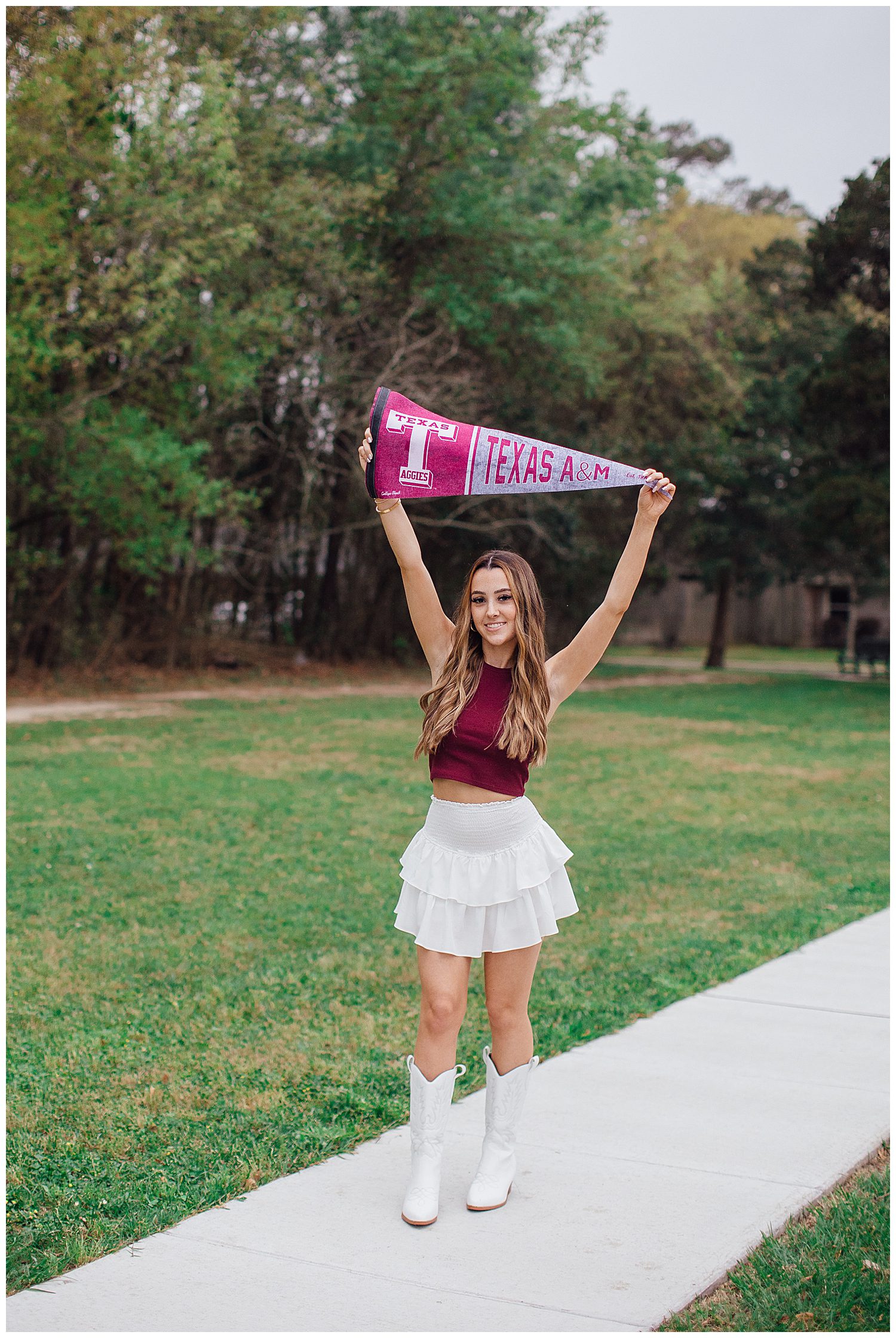 senior girl in white skirt and boots and maroon shirt standing in a outdoor park holding Aggie sign over her head